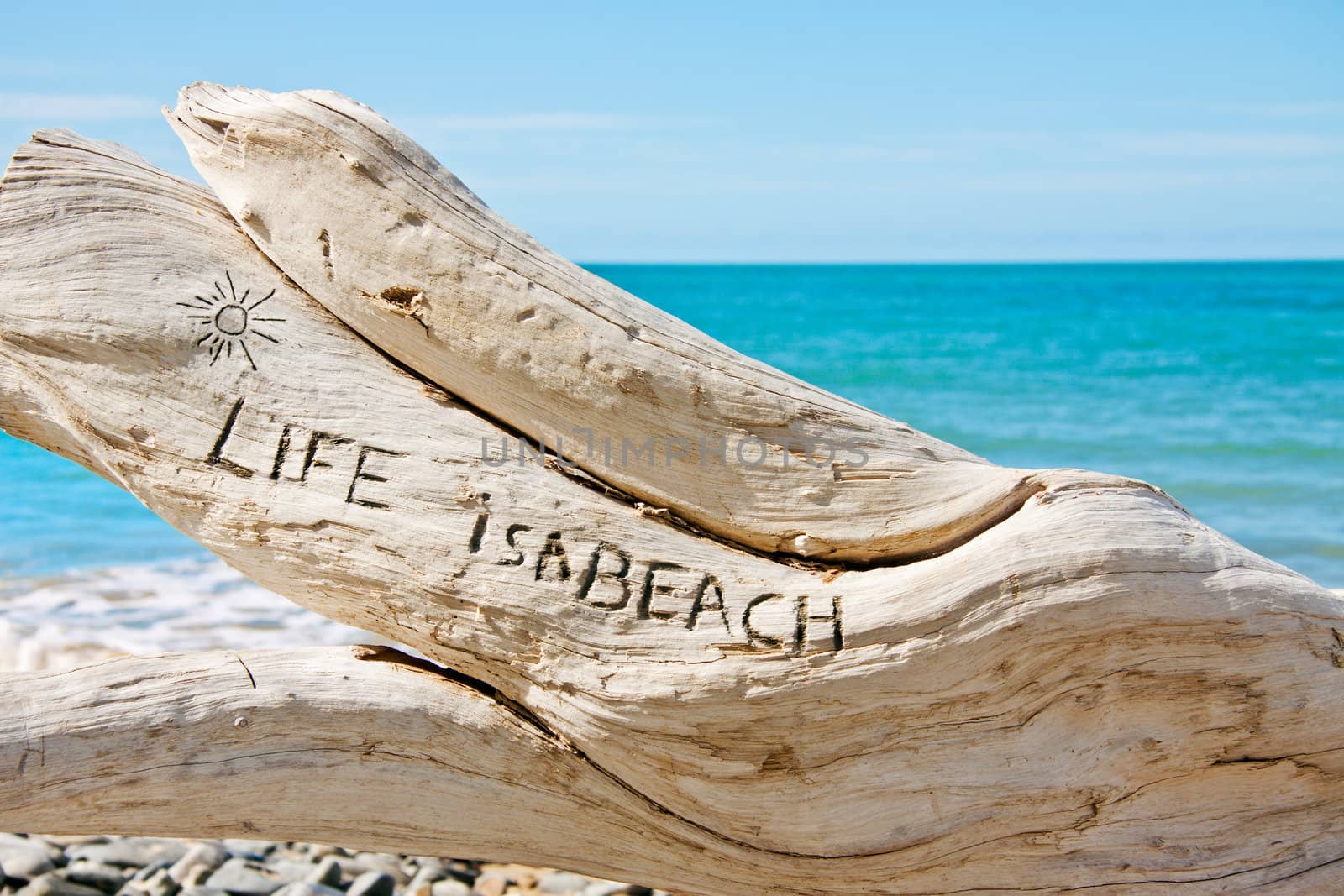 A log on a beautiful tropical beach with the words: 'Life is a beach' written on it.