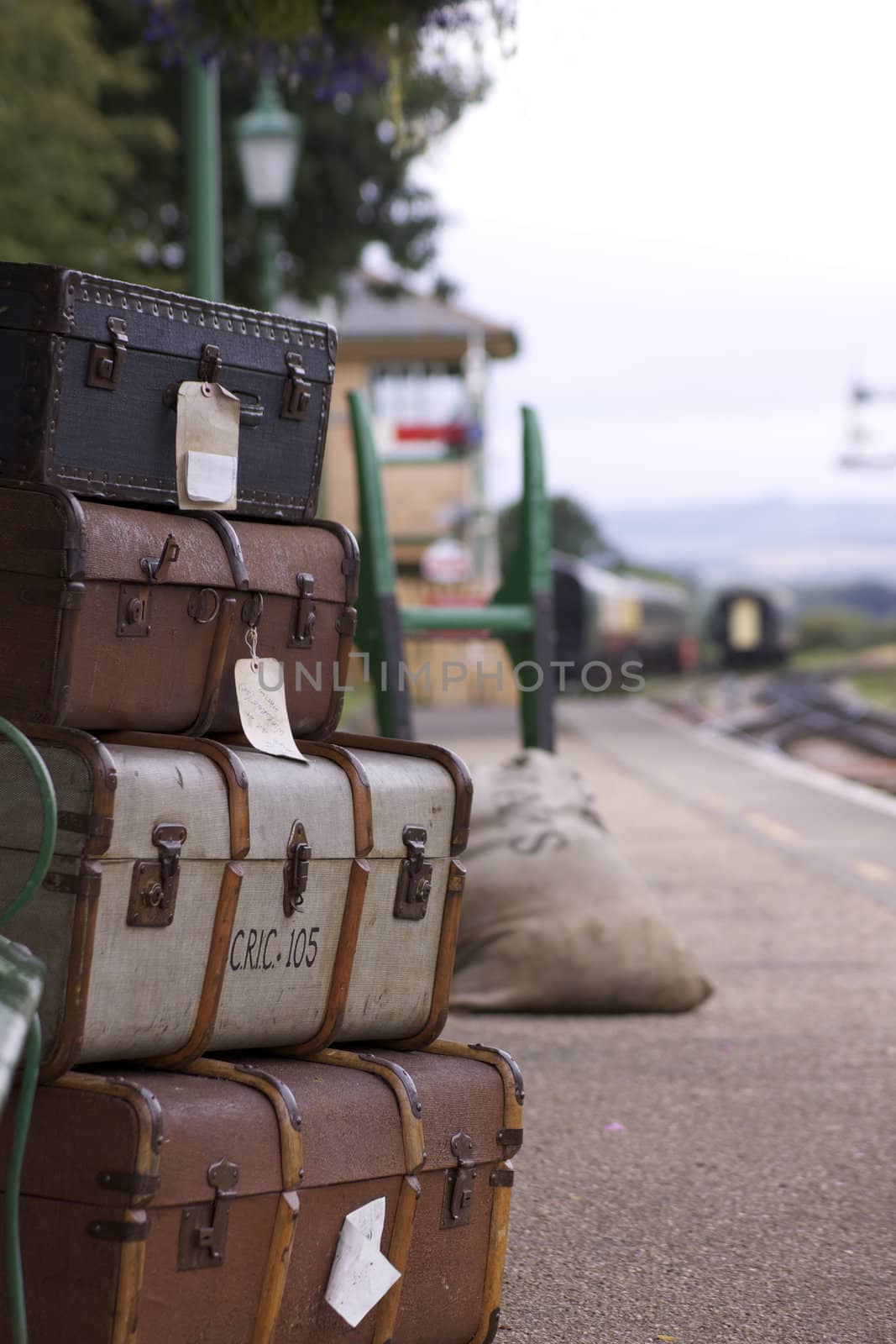 A set of labeled period luggage consisting of old leather cases, set on a trolly on the platform of a retro railway station. Location at Harmans Cross station on the Swanage steam railway network in Dorset. The stations signal box and carriages in soft focus to the background.