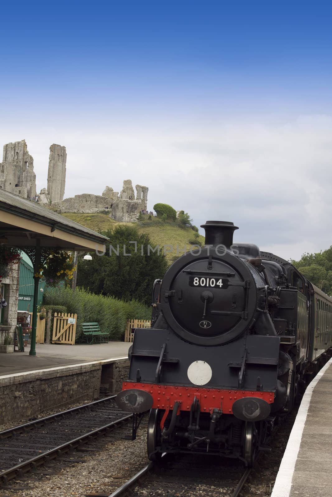 A steam train arriving at Corfe Castle Railway Station, on the Swanage railway service. Located in Dorset, Hampshire. The ruins of Corfe Castle visible in the background.