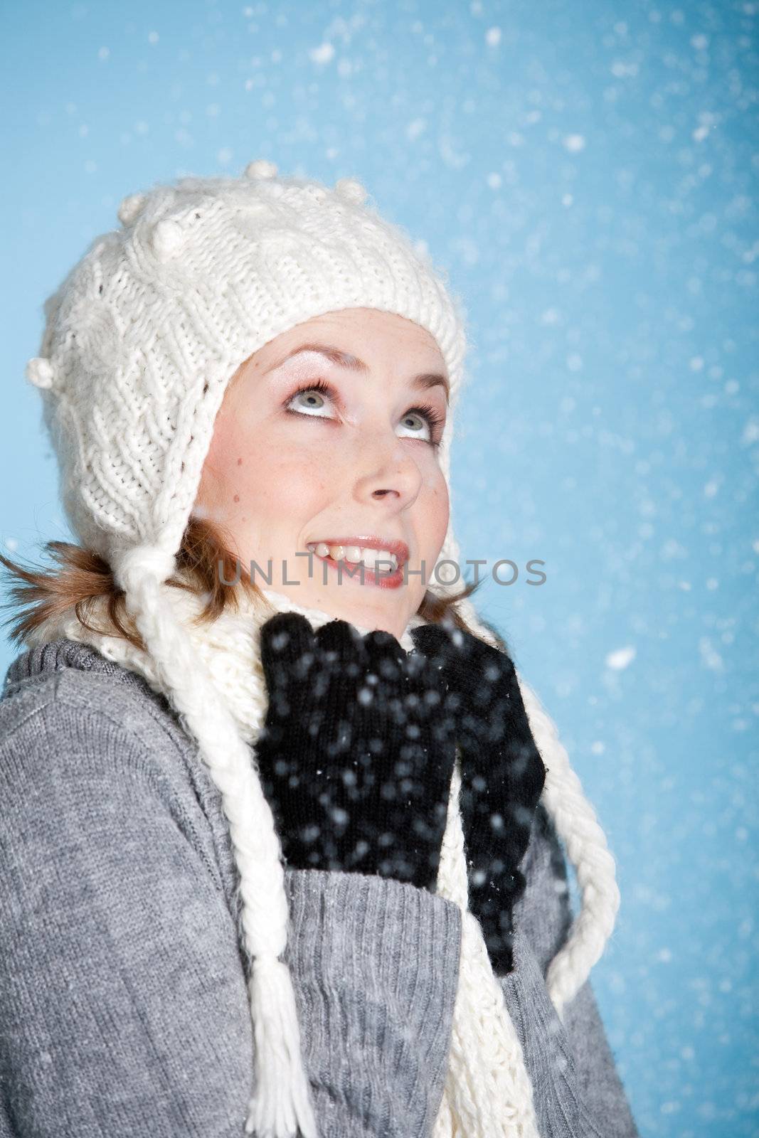 Happy blond girl warmly wrapped up looking up at the snow