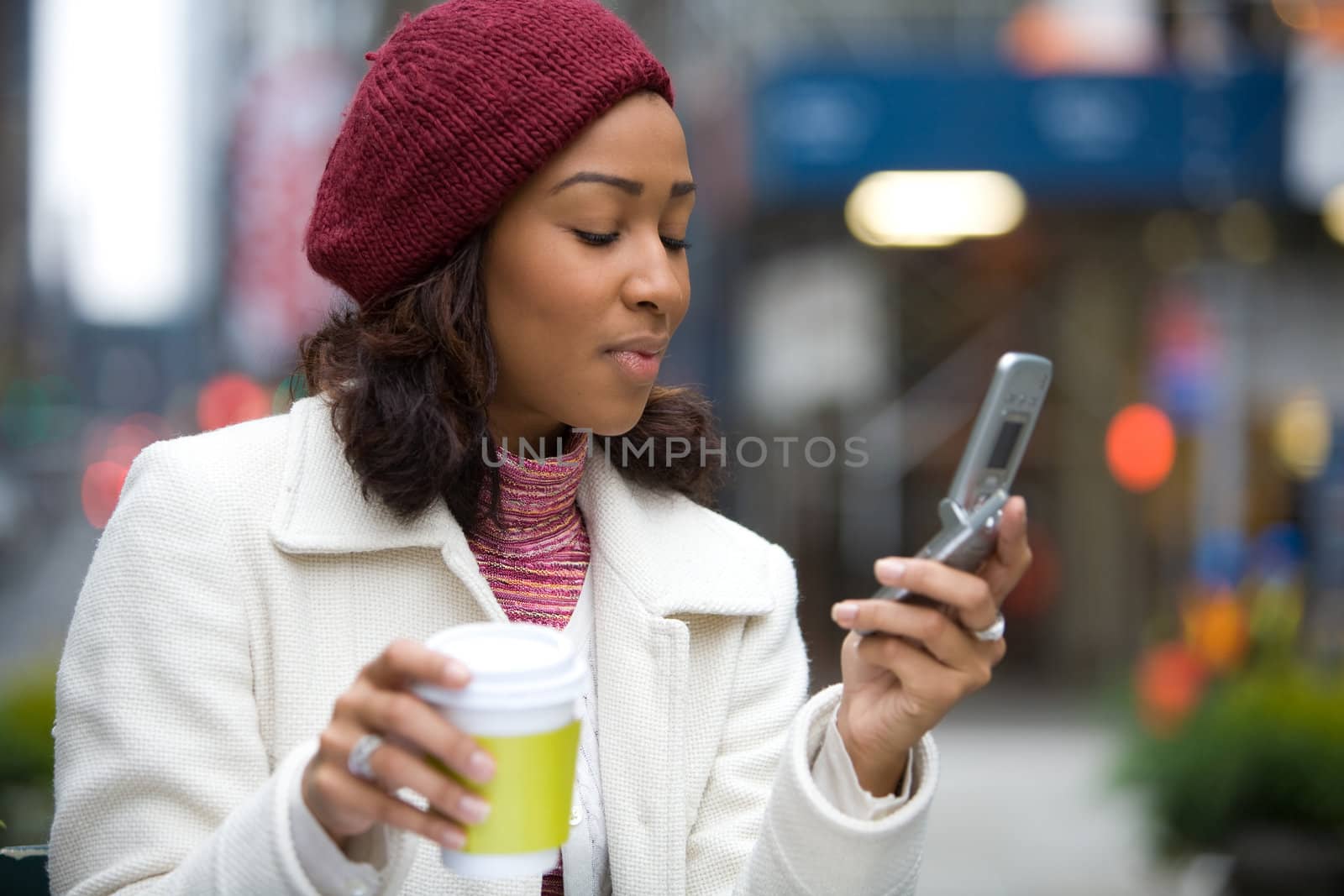 An attractive business woman checking her cell phone in the city.  She could be text messaging or even browsing the web via wi-fi or a 3g connection.