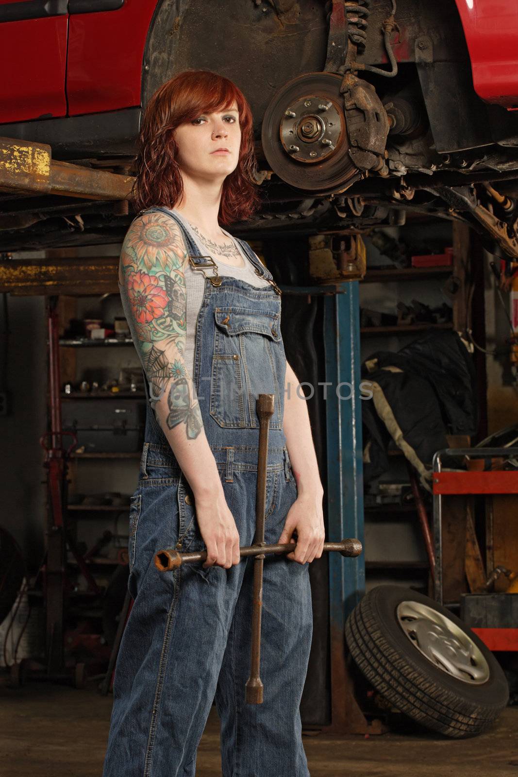 Photo of a young beautiful redhead mechanic wearing overalls and holding a huge wrench.  Attached property release is for arm tattoos.