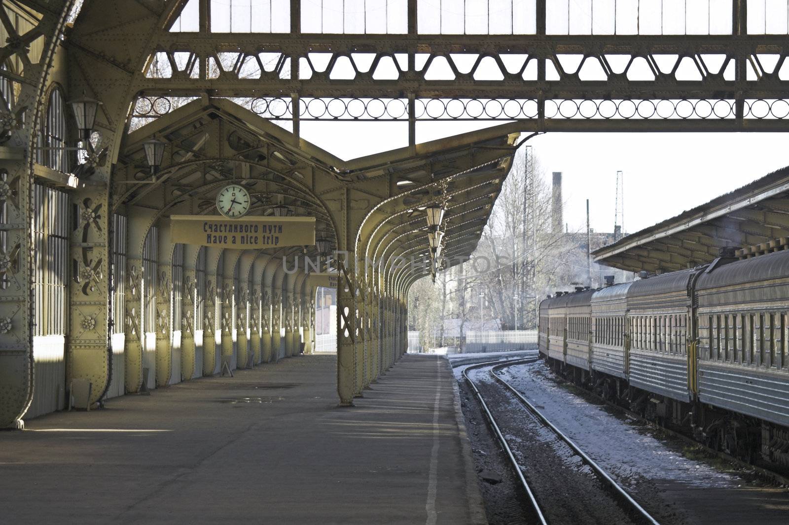 Railroad station platform with a hanging clock and "Have a nice trip" signboard.