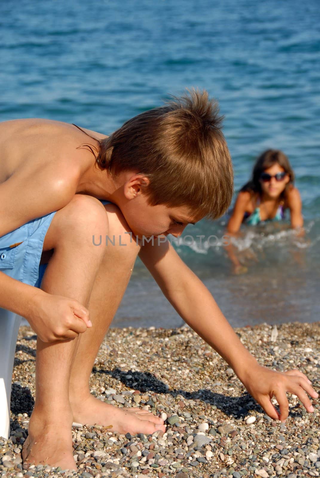 little boy playing with rocks on pebble beach by blue sea