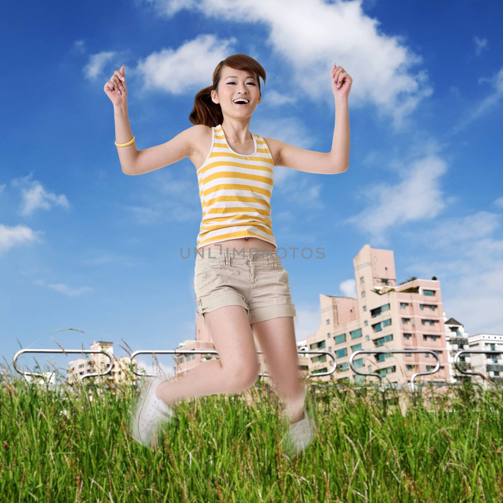 Happy girl jump in park with green grass under blue sky.