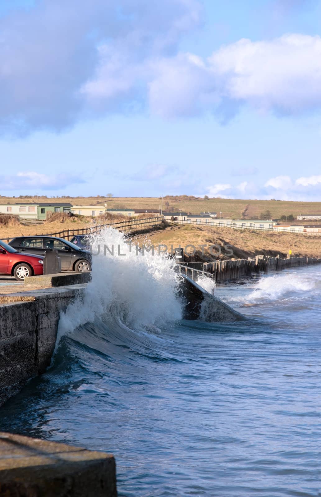 waves splashing against a coastal wall during a storm with cars and homes in background