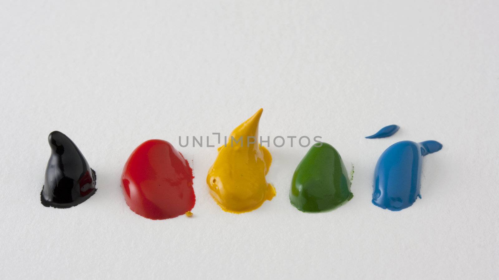 five dabs of watercolor paint (black, red, yellow, green, blue) on white textured paper