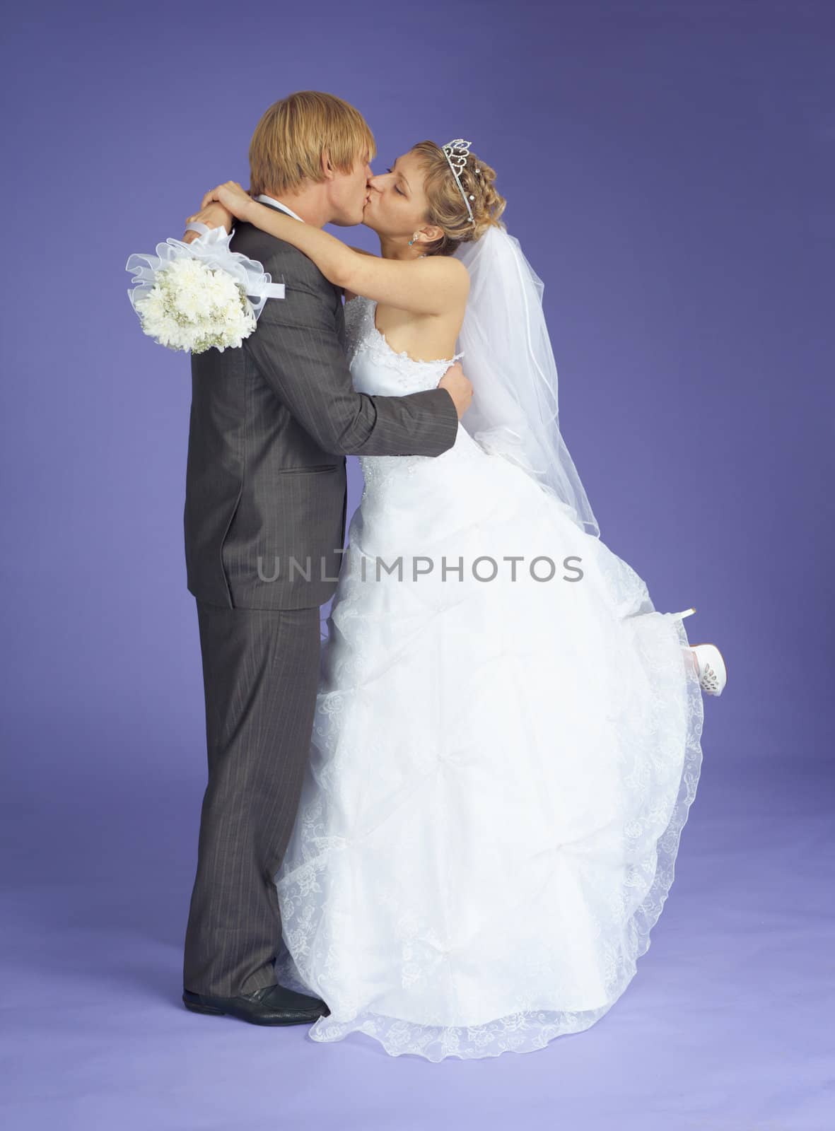 Newly-married couple kisses standing on a violet background