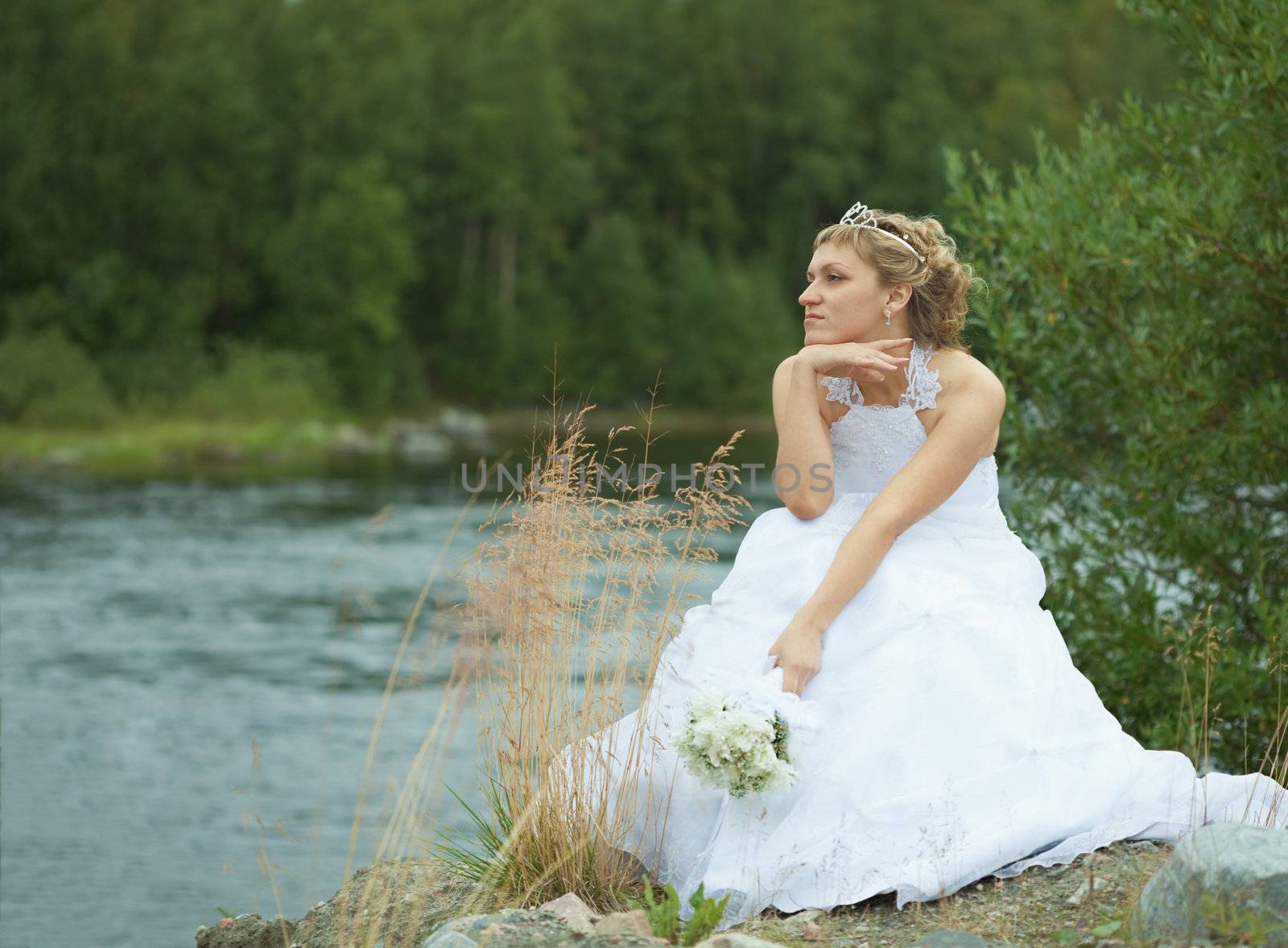 The sad bride sits on river bank and looks afar