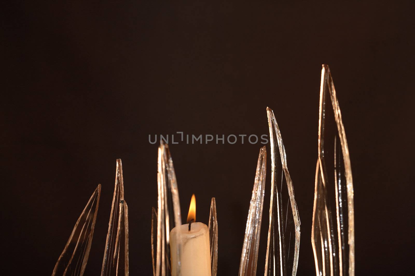 Closeup of few pieces of cracked glass and lighting candle on dark background