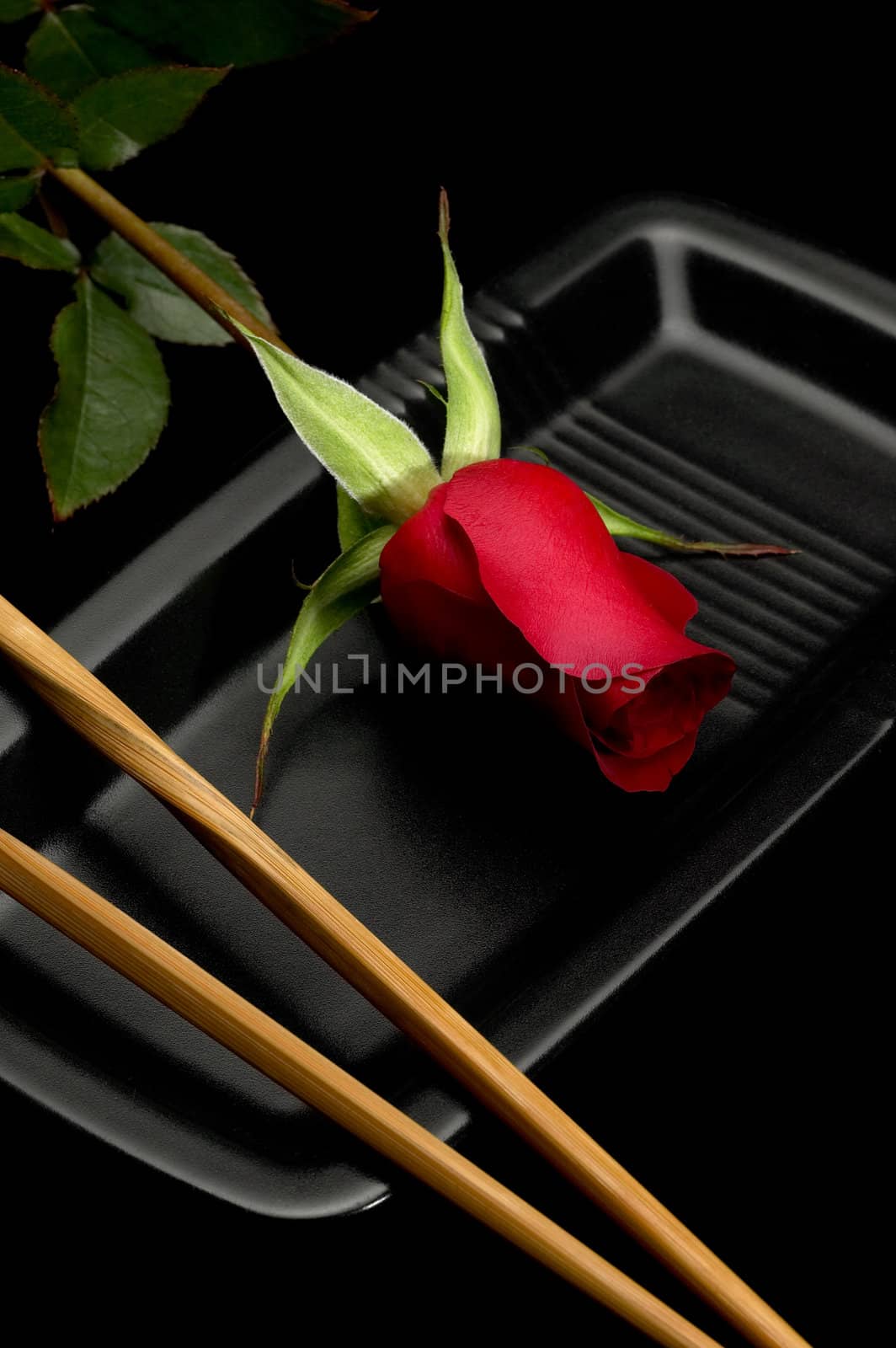 red rose on a japanese black plate with chopsticks over black