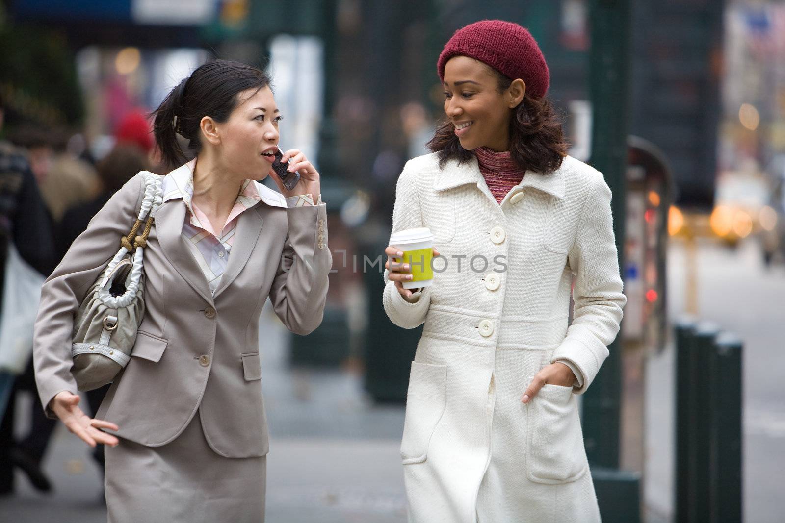 Two business women walking in the big city. One is on her cell phone.