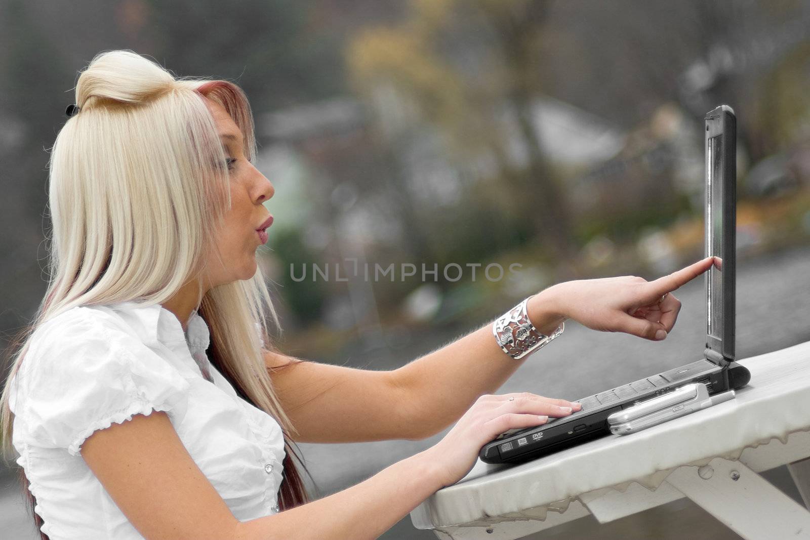 A beautiful young blonde woman points to her laptop screen in amazement.  It looks as if she is seeing something offensive.