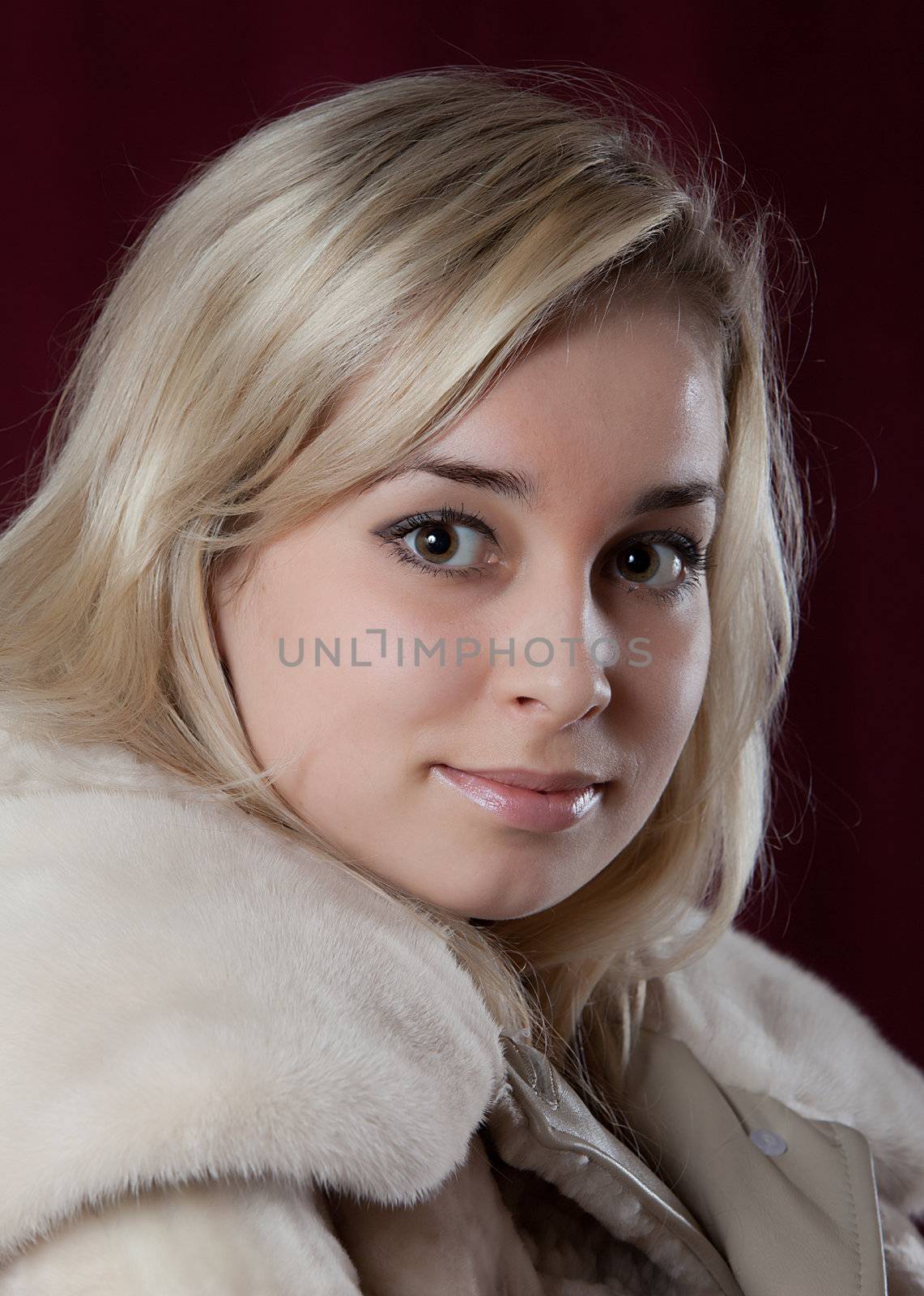 Portrait of the young beautiful girl in a fur coat on a dark background