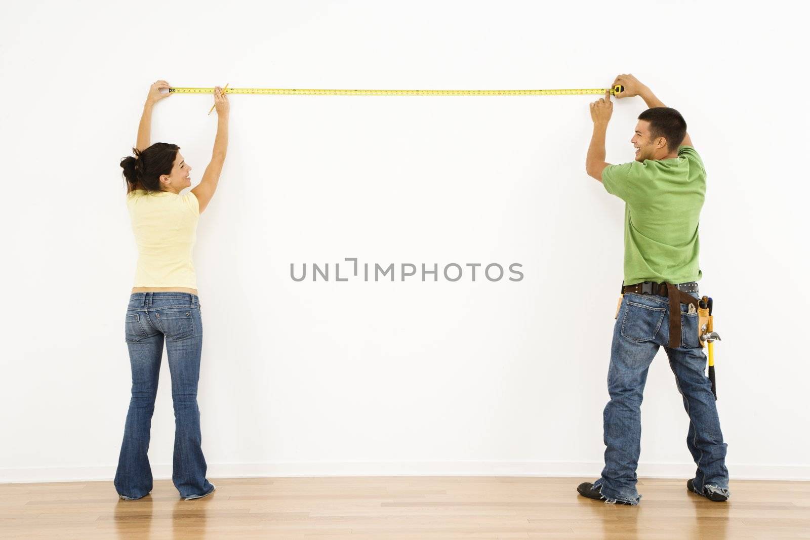 Couple measuring interior wall and smiling.