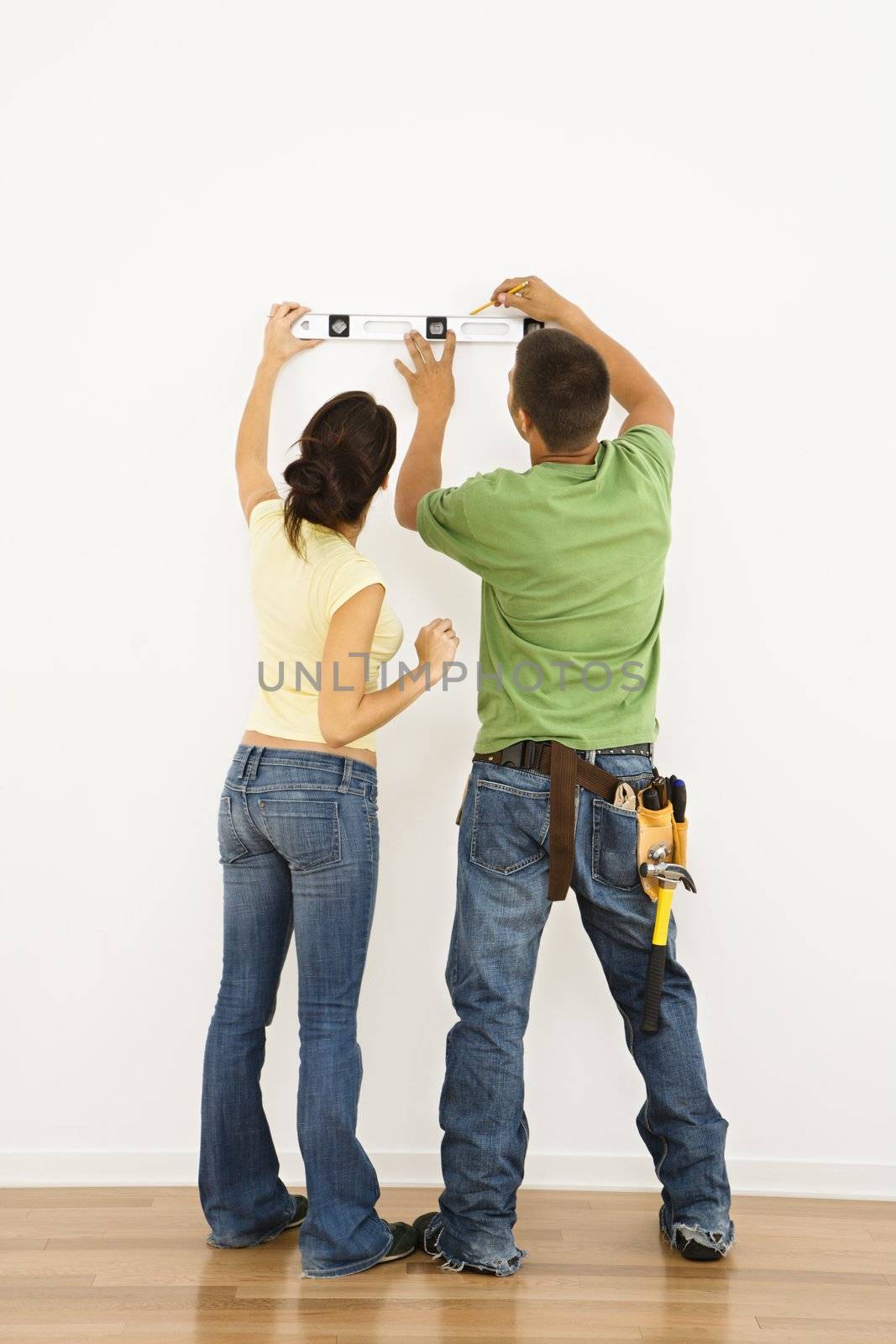 Couple holding level to interior wall and marking with pencil.