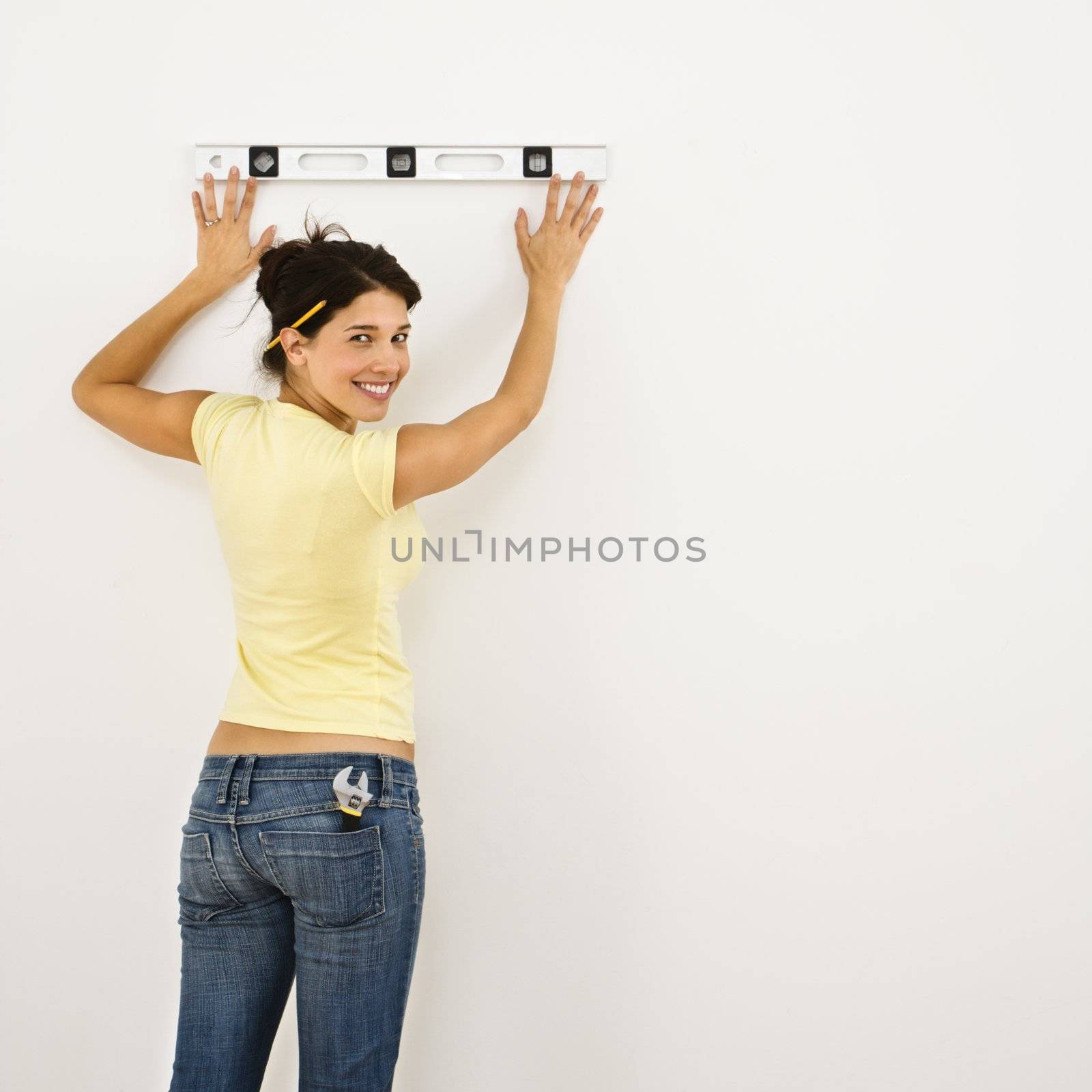 Woman standing holding level up to interior wall and smiling.