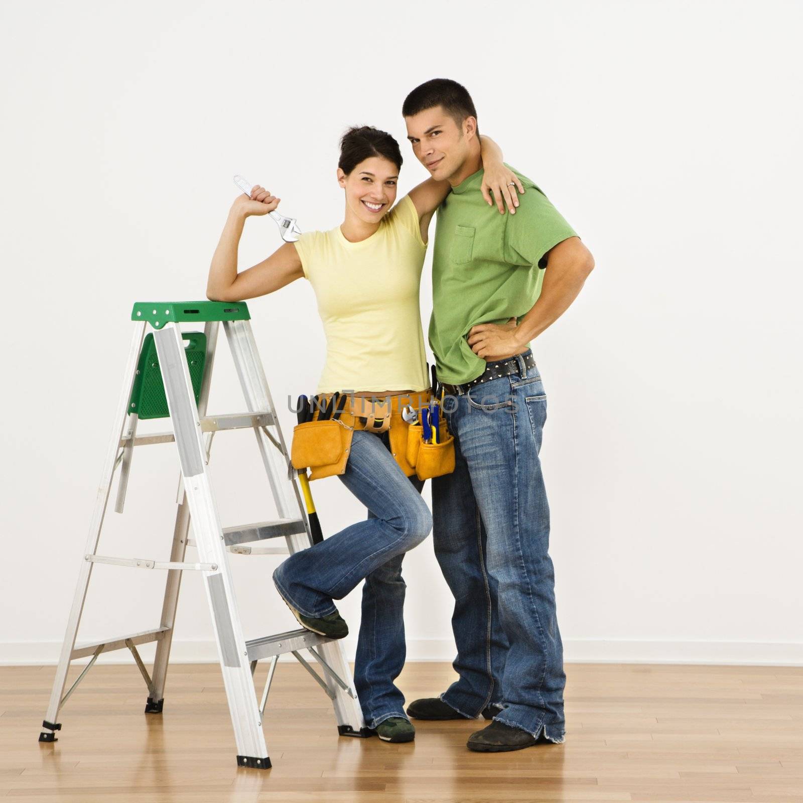 Couple with tools and ladder standing in home smiling.