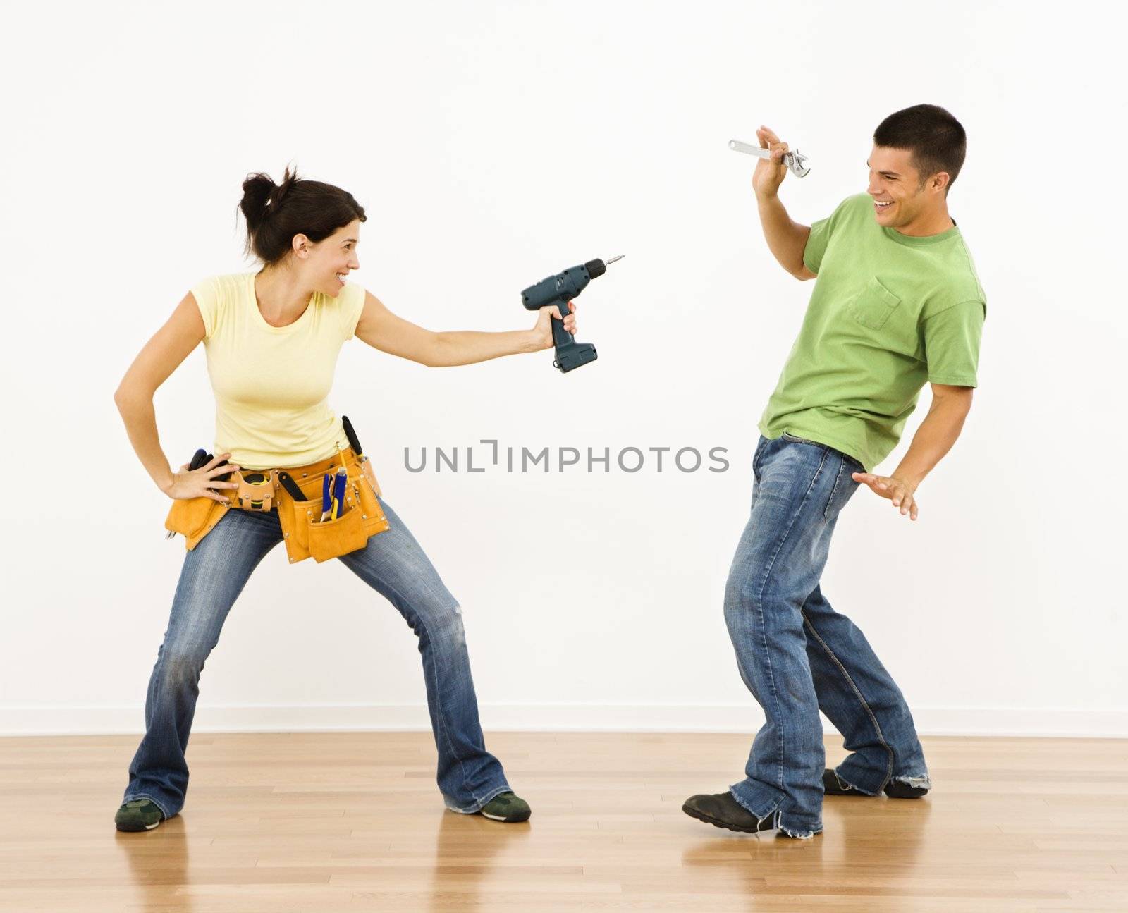 Woman pointing drill playfully at man smiling and laughing in home.
