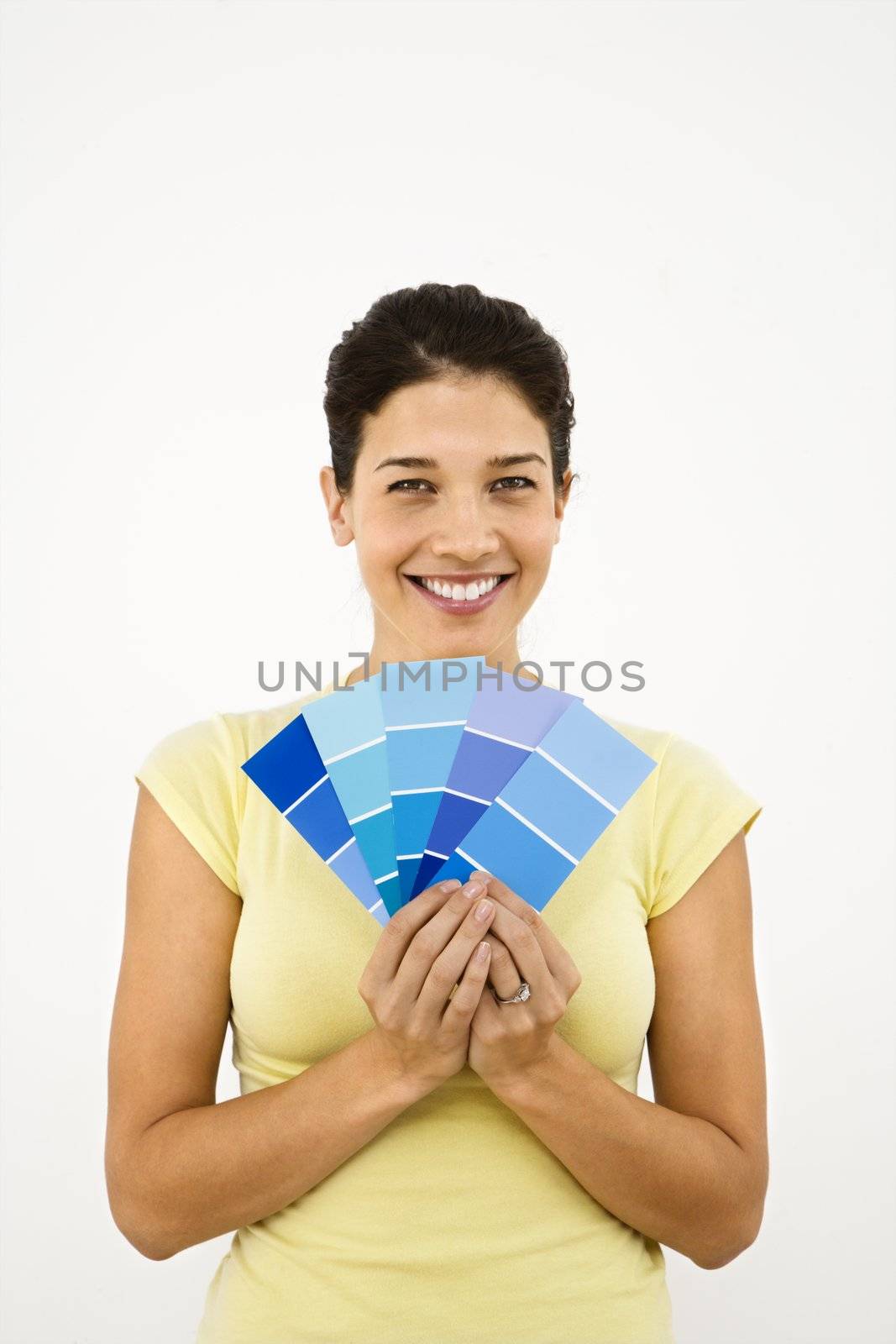 Pretty smiling woman holding paint sample cards in front of white wall.