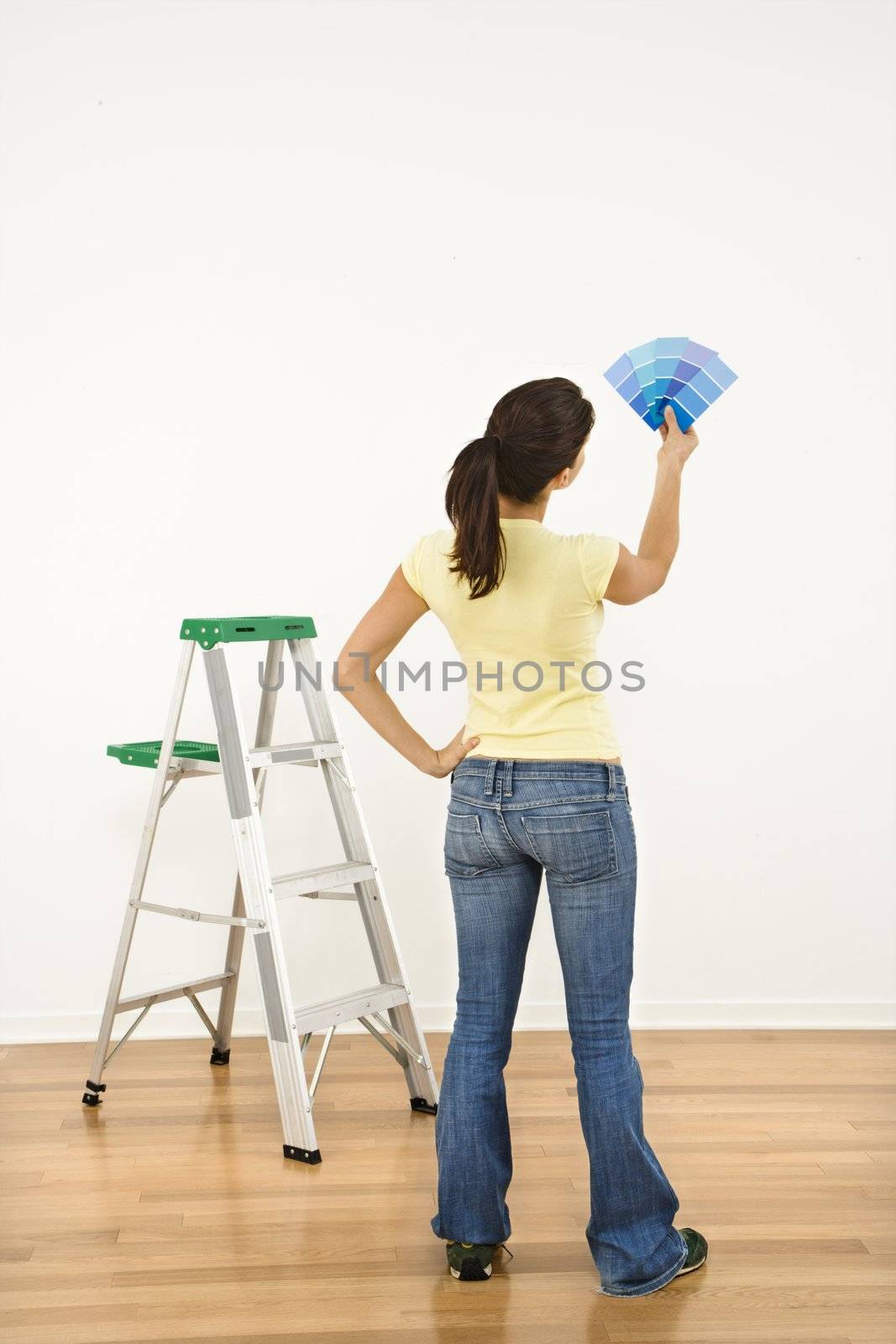 Woman standing in front of white interior wall with paint sample cards trying to choose color.