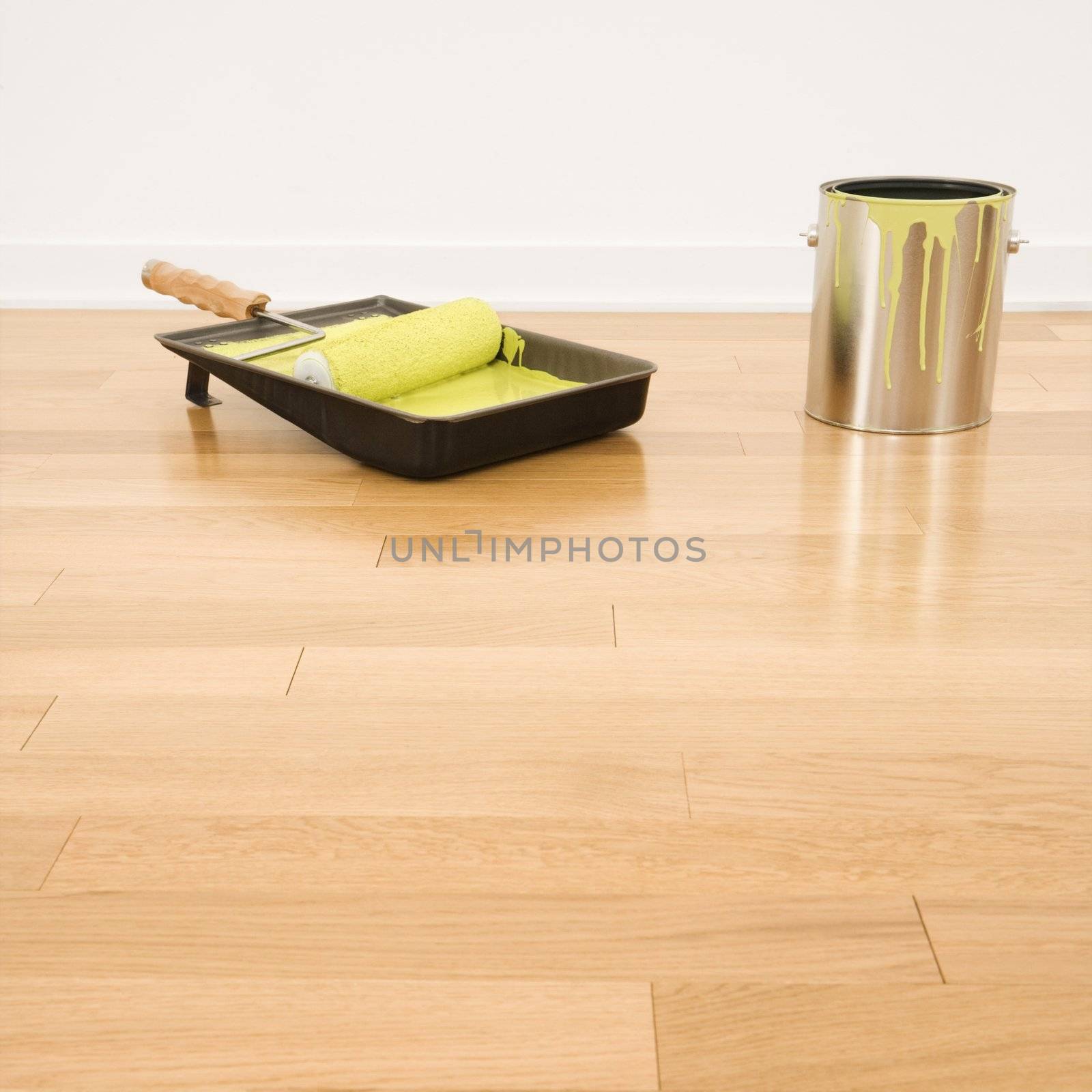 Still life of paint roller in tray with paint can on wood floor.