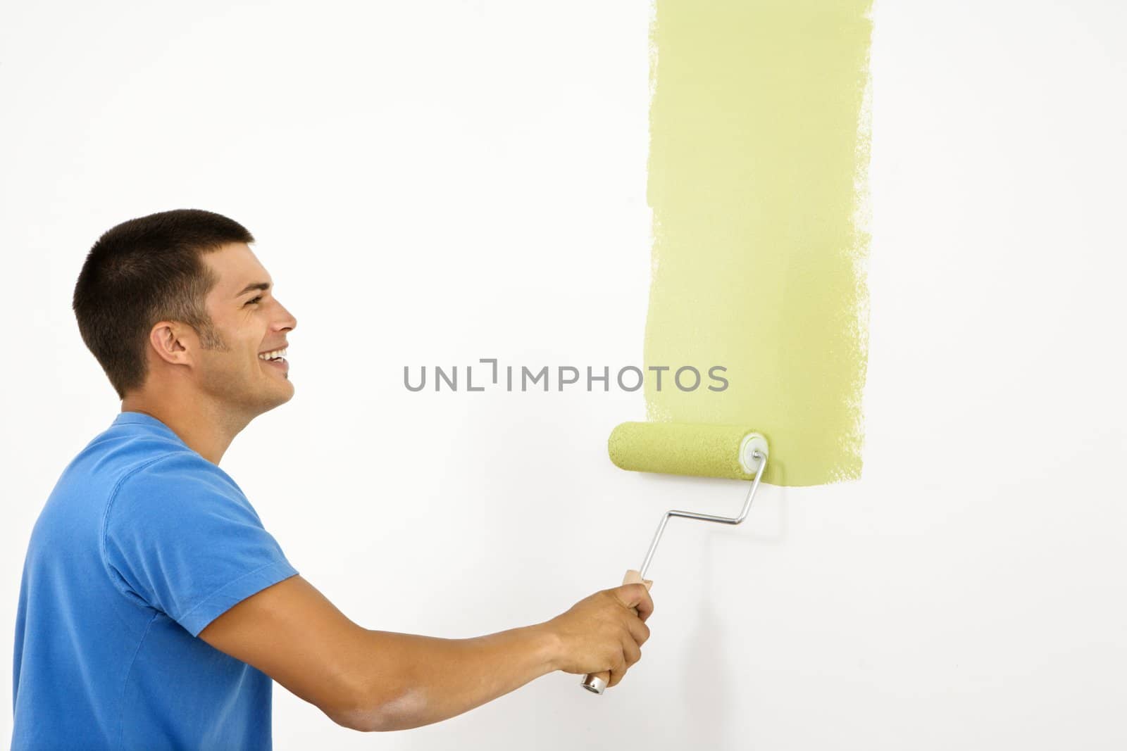 Attractive smiling man painting white wall with green paint.