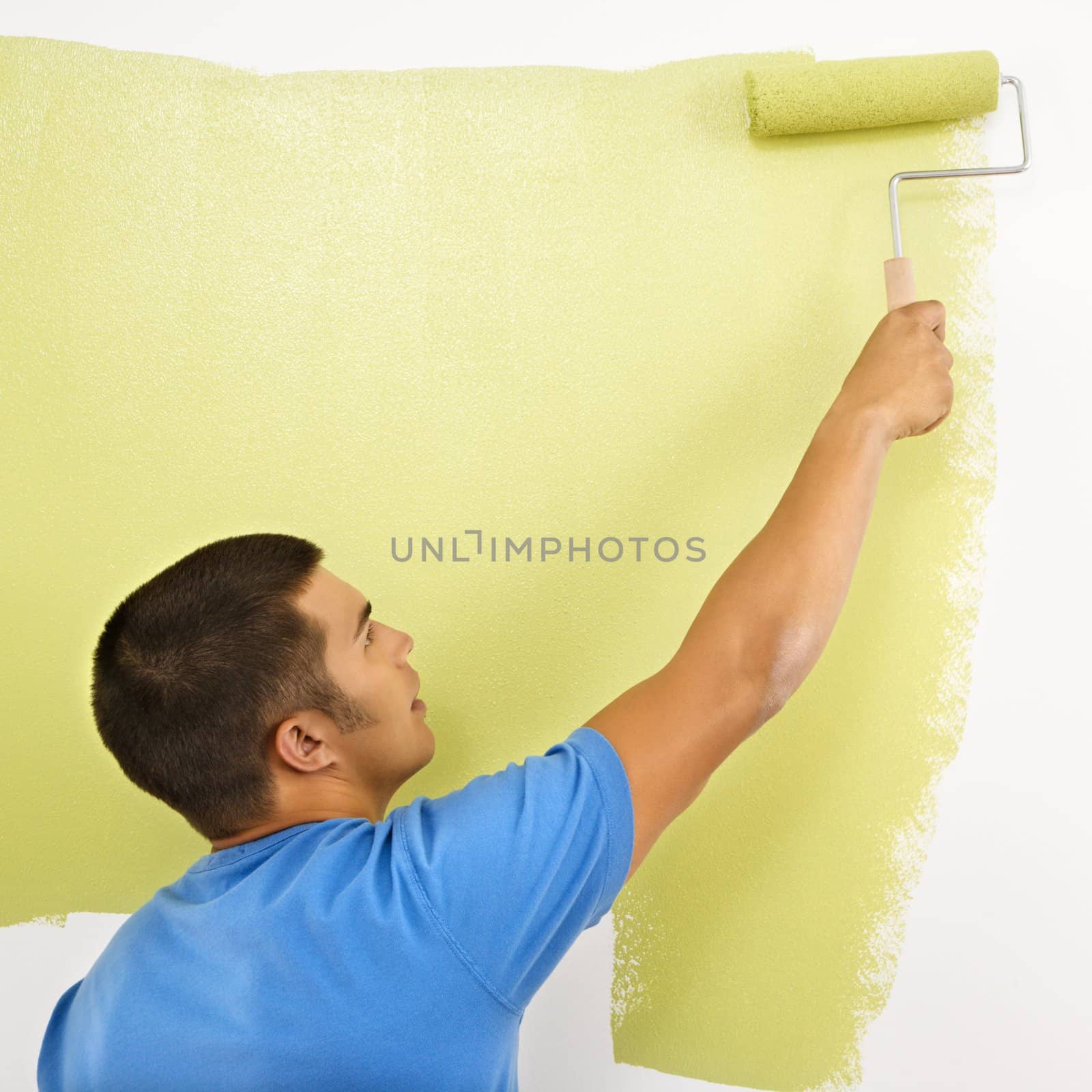 Man painting over white wall with green paint using paint roller.