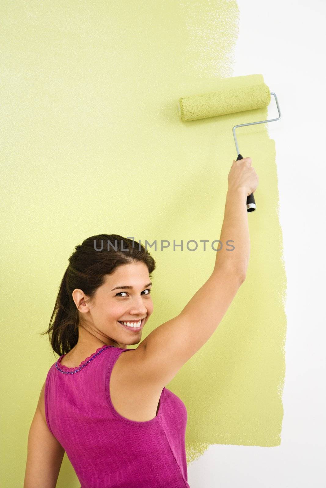 Pretty smiling woman painting interior wall of home with paint roller.