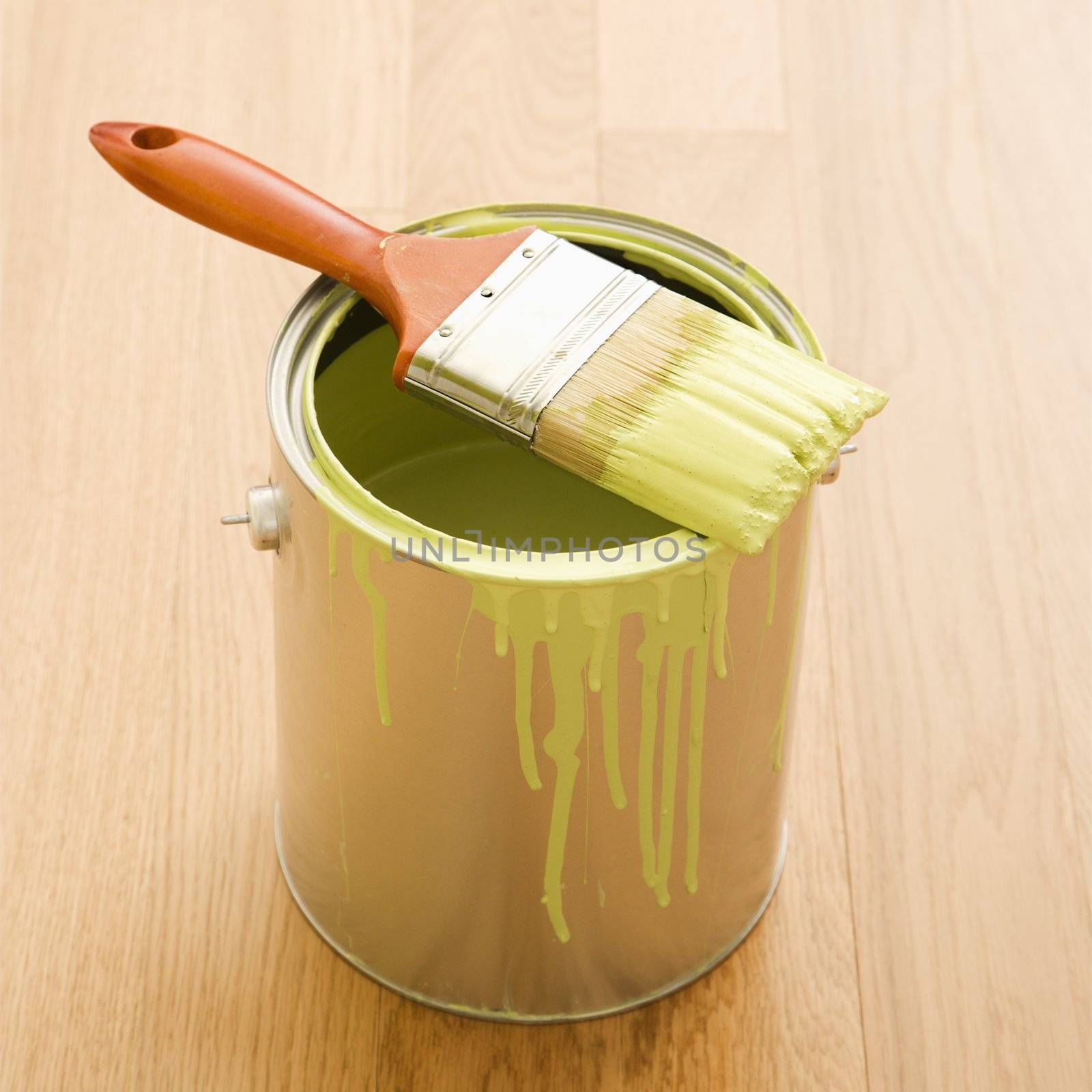 Paintbrush resting on paint can on wood floor.