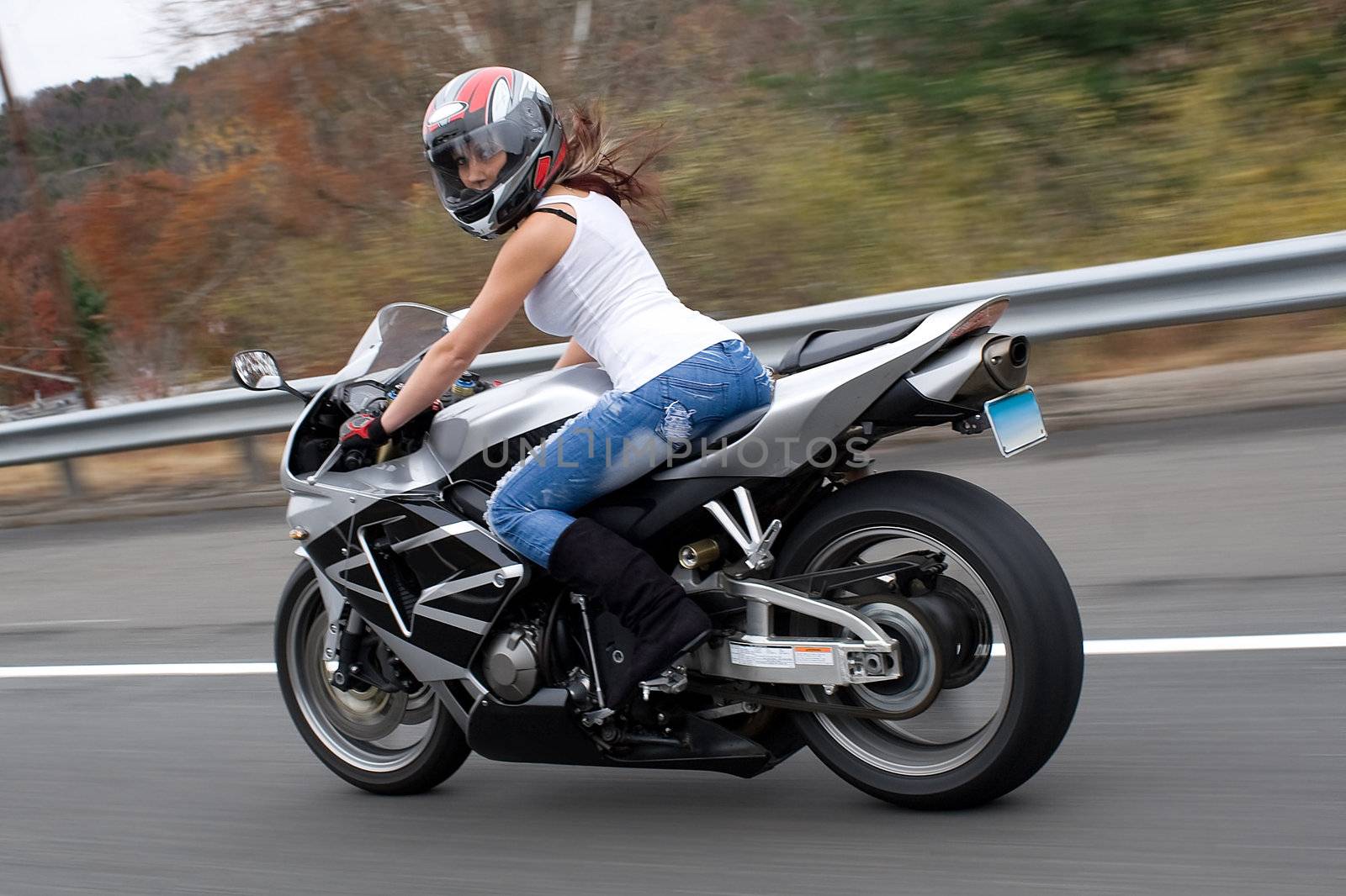 A pretty blonde girl in action driving a motorcycle at highway speeds.