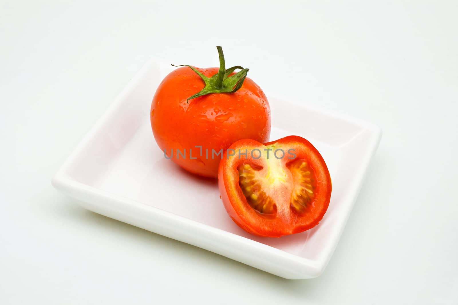 Tomoato on plate, white background, with drops of water.