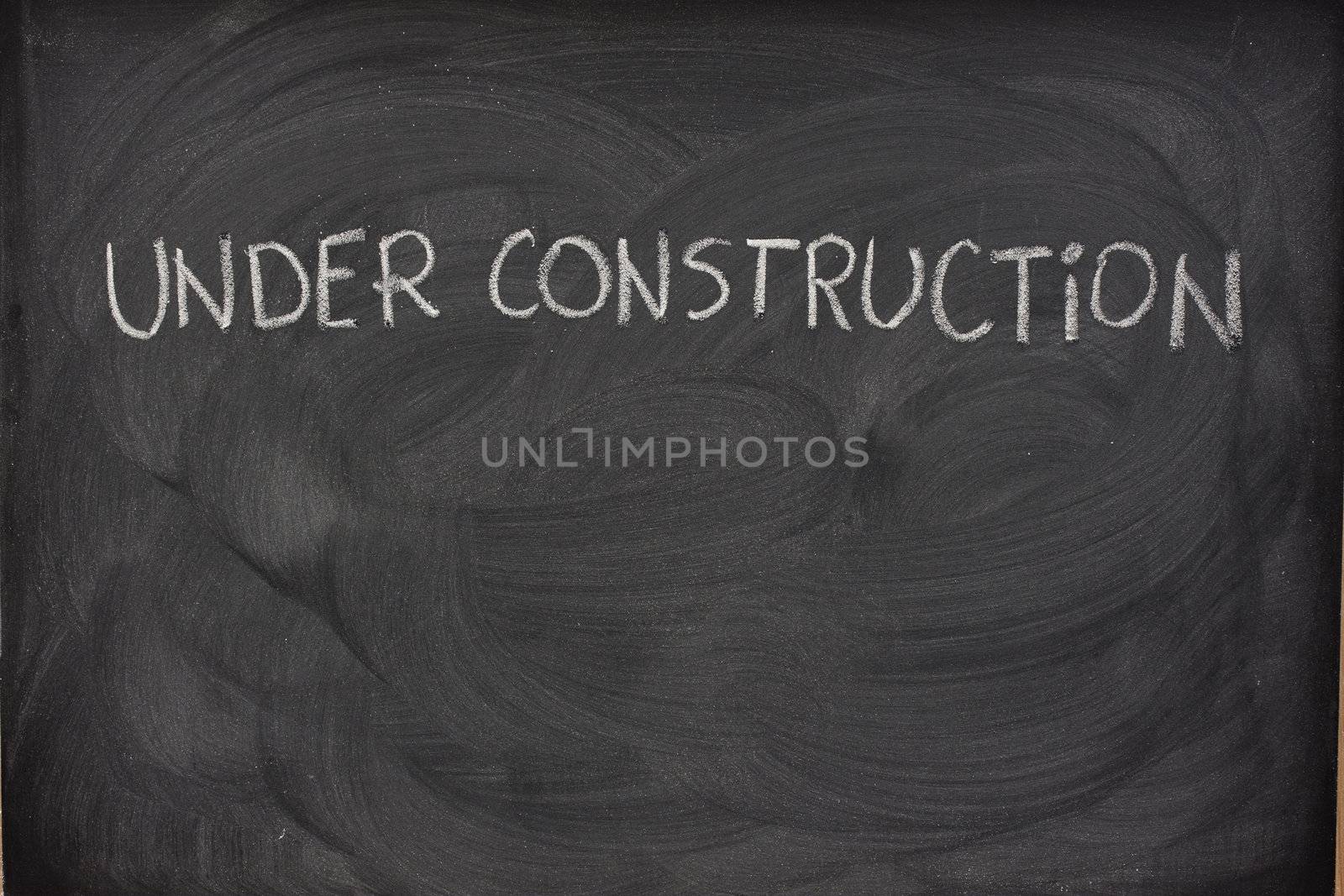 under construction phrase handwritten with white chalk  on a blackboard with eraser smudges and copy space below