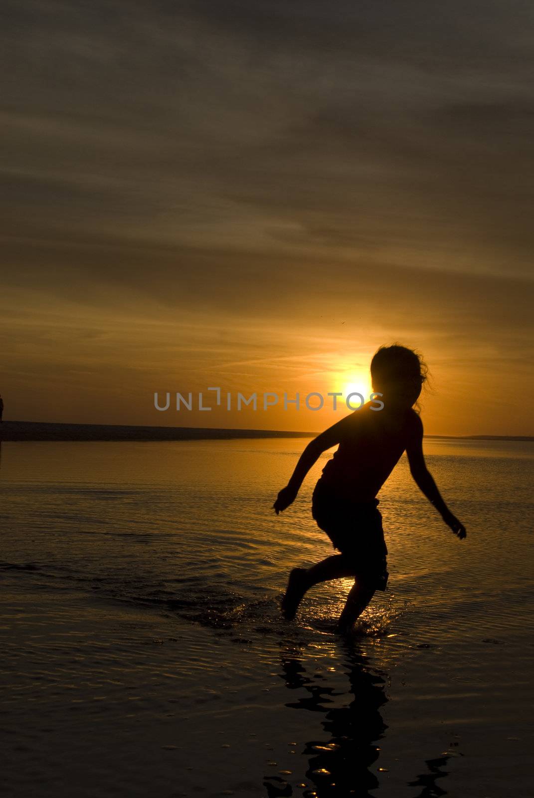A young girl playing in a wading pool at the beach as the sun sets behind her