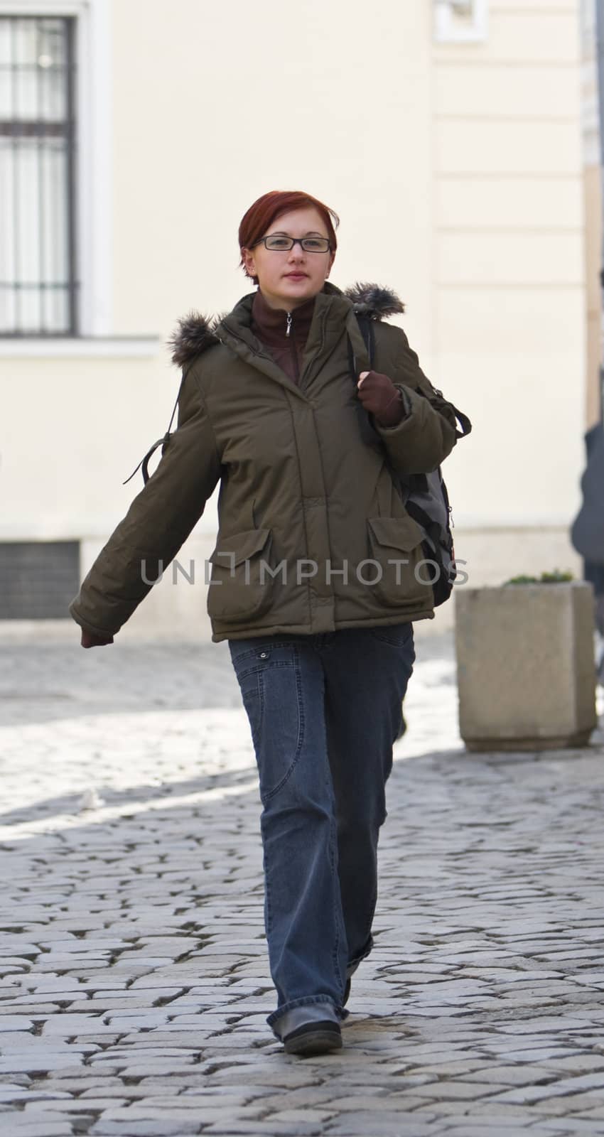 Redheaded girl student walking on a paved street.