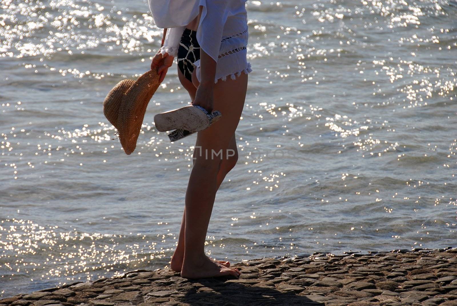 woman in swim suit with hat standing by shining seawater