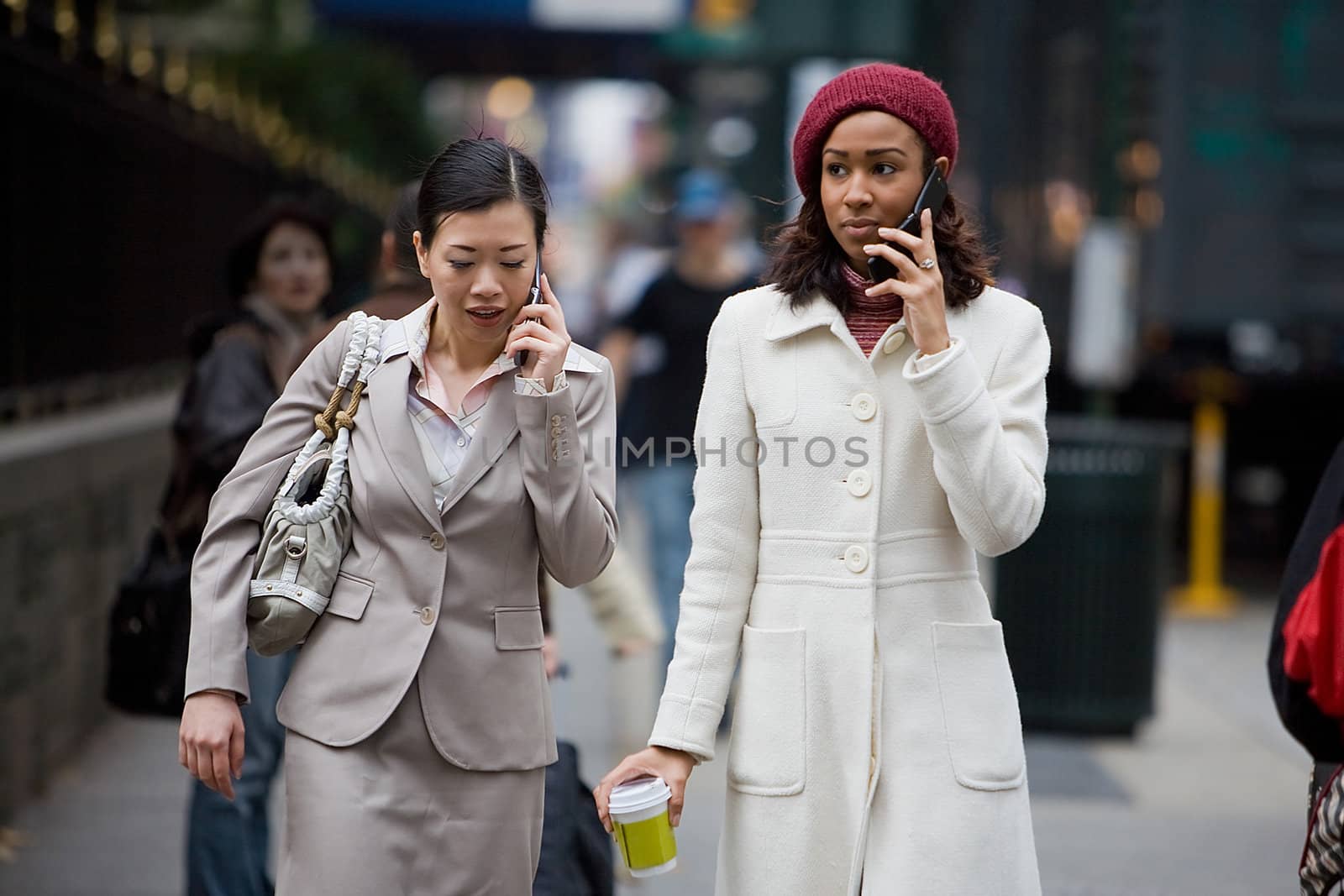 Two business women having conversations on their cell phones while walking in the big city. 