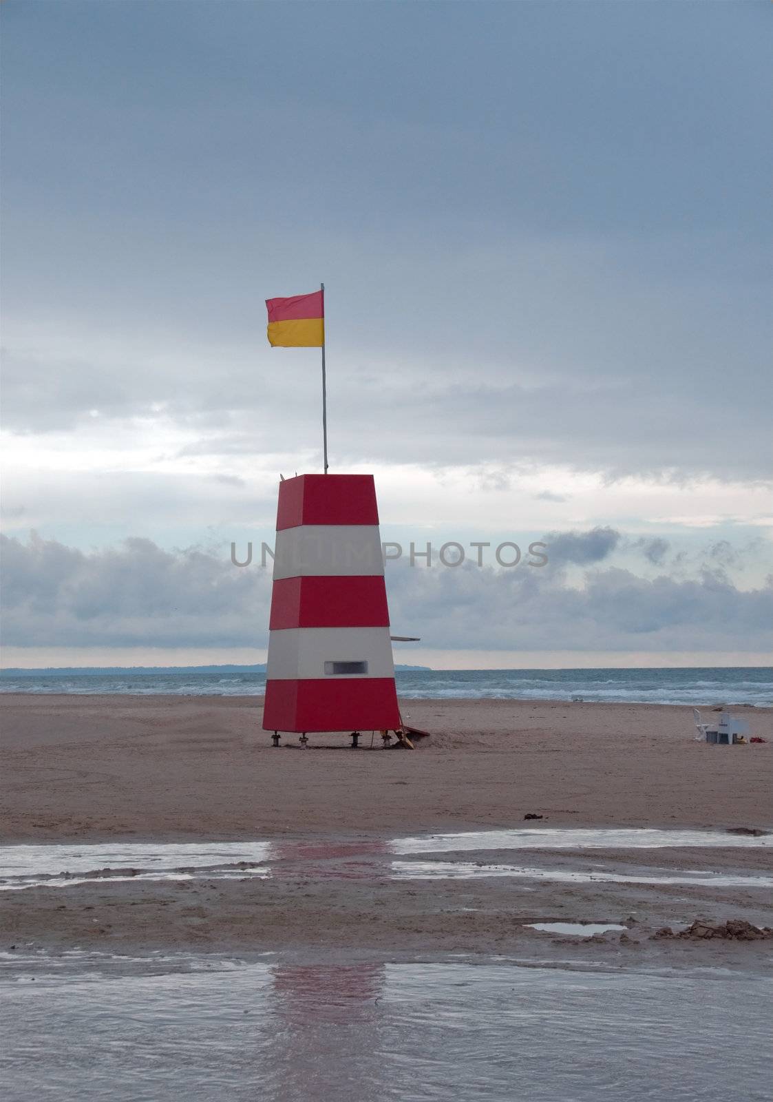 A red and white tower with lifeguard flag on a beach