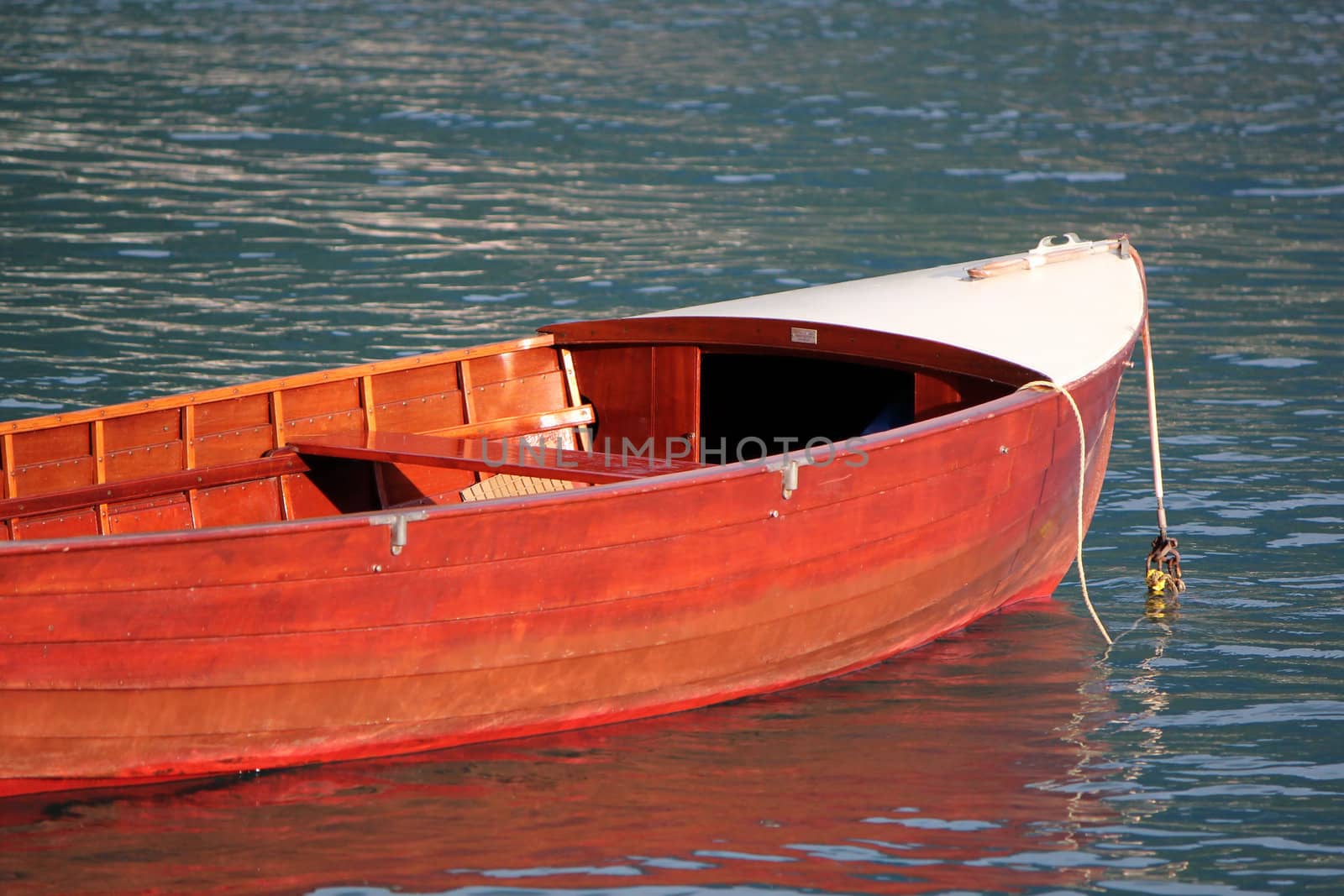 Small red wood boat floating on the water by sunset
