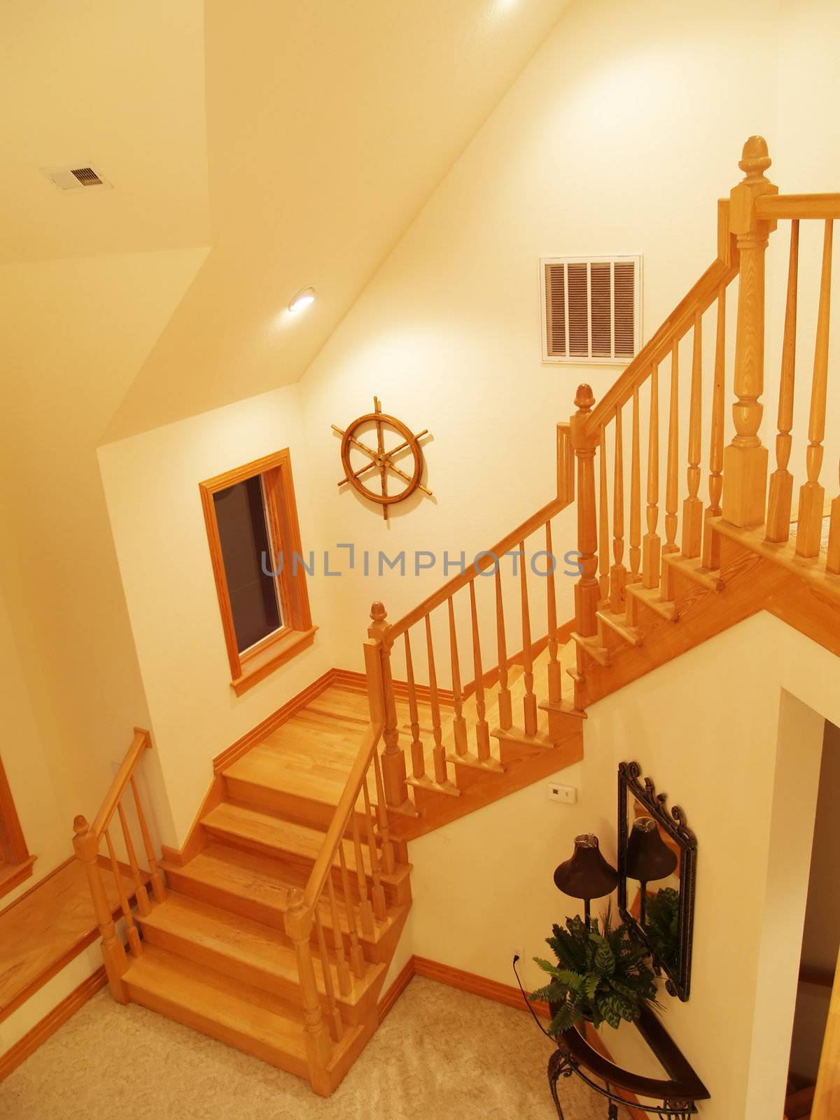 Wooden staircase and railing leading up to a loft in a beachfront residence. A ship's wheel hangs on the wall.