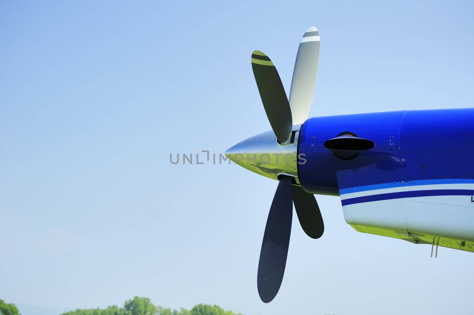 The propeller of an aircraft against a clear blue sky. The grass airstrip and sky can be seen reflected in the nose cone. Space for text in the blue sky.