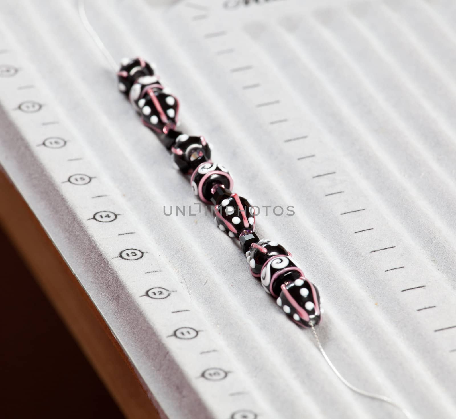 Making handmade jewelry with black, white and pink beads being threaded on a string