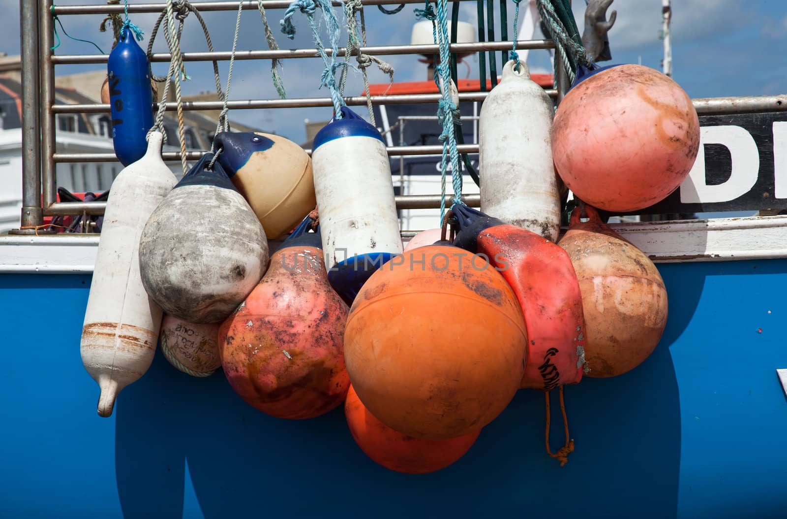 Group of colored plastic floats on side of blue boat used as bumpers