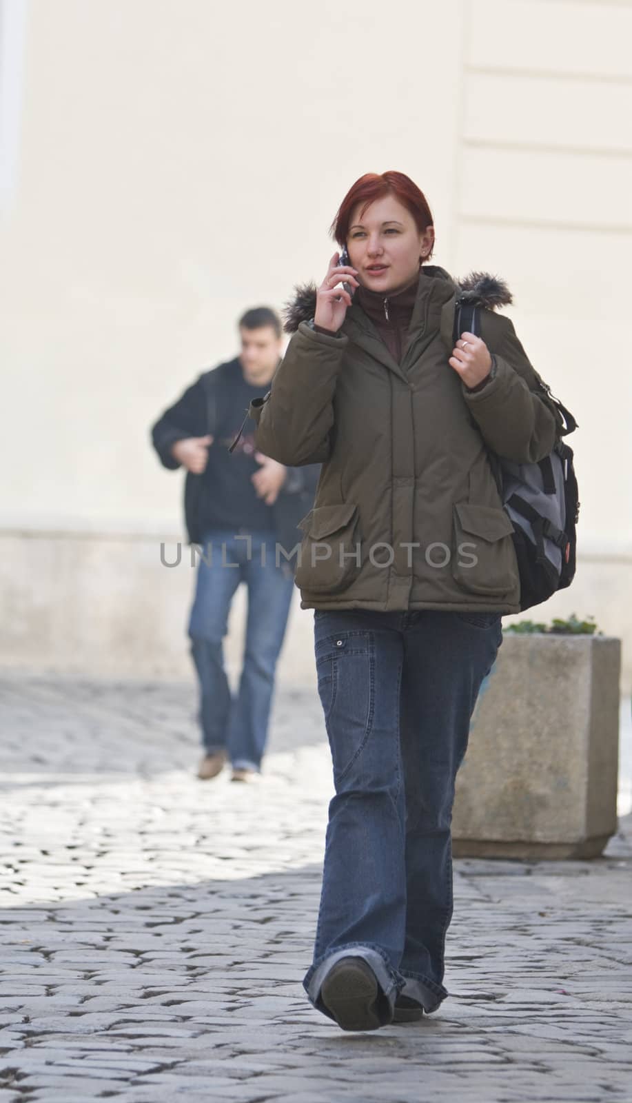 Redheaded girl student at the phone while is walking on a paved street.