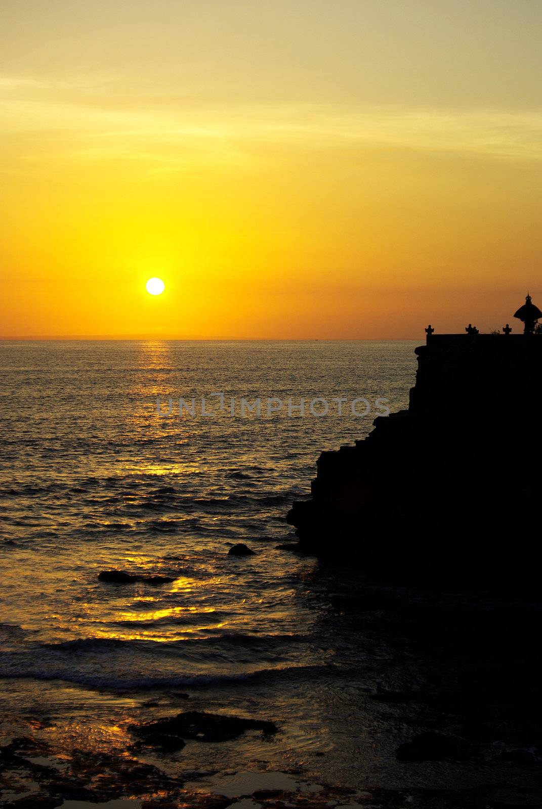 It's a beautiful sunset on Bali island with a little temple in the shadows