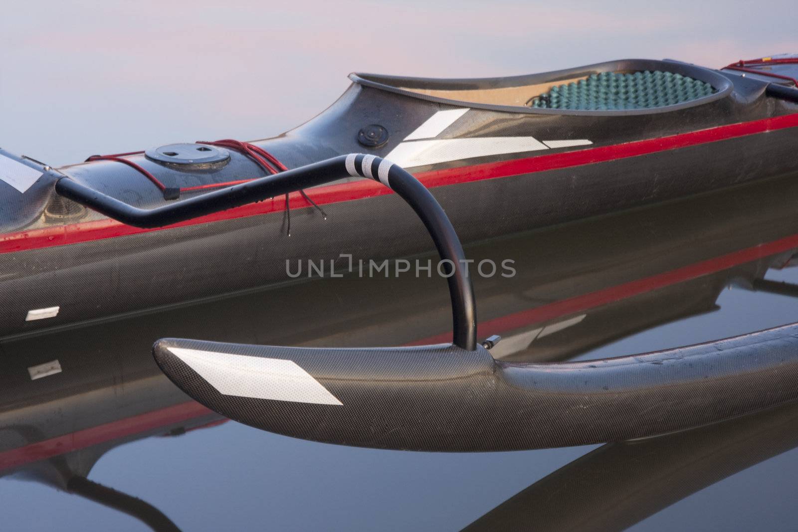 cockpit of racing outrigger canoe (black carbon fiber design) with ama in front on calm water with reflection
