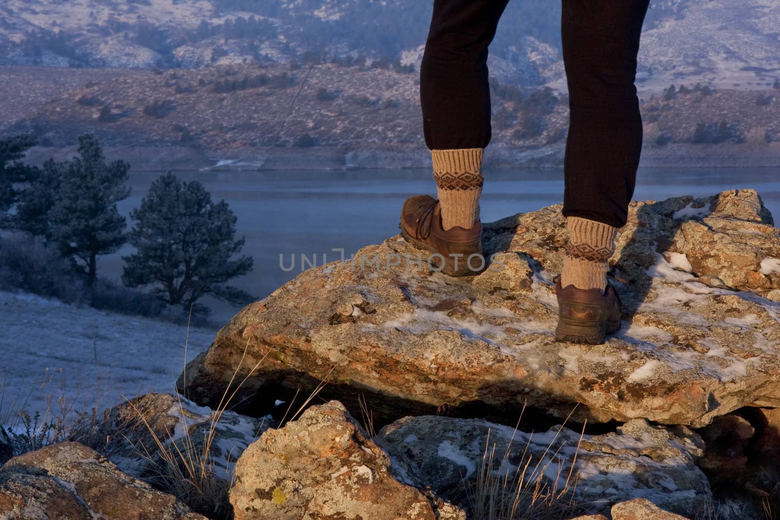 hiker or trail runner legs and feet on rock overlooking mountain lake,  winter scenery with snow, fog, frost at sunrise light in Colorado