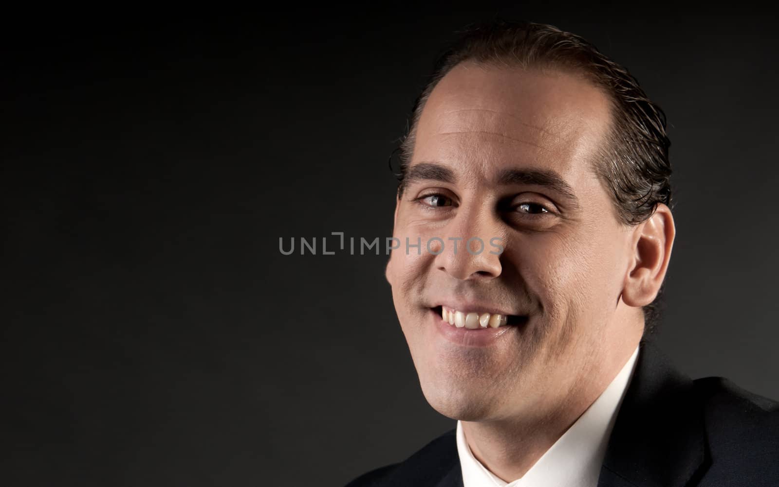 Adult businessman closeup portrait smiling on dark background.