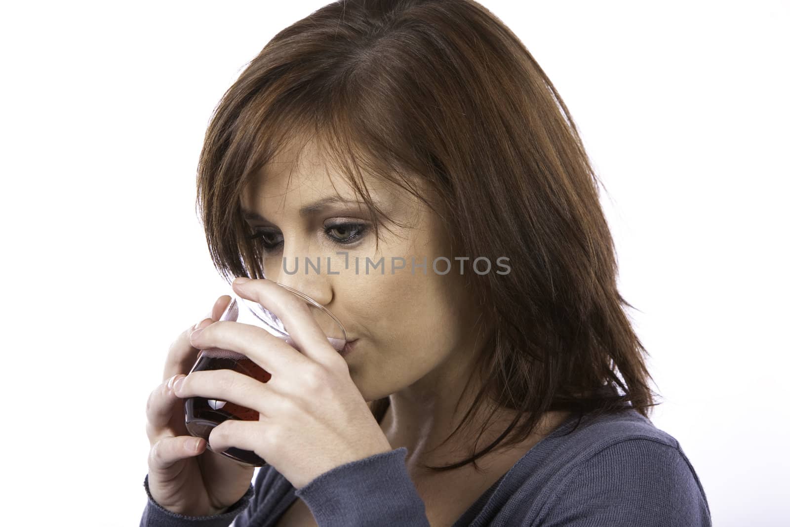 A beautiful young woman with red hair drinking a red fizzy drink from a glass