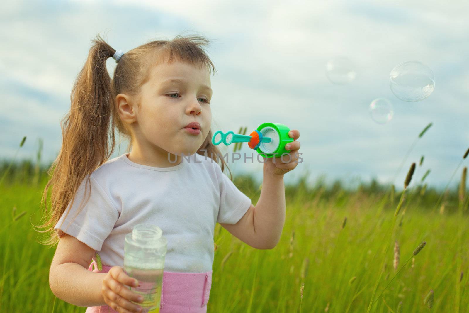The little girl starts soap bubbles in the field
